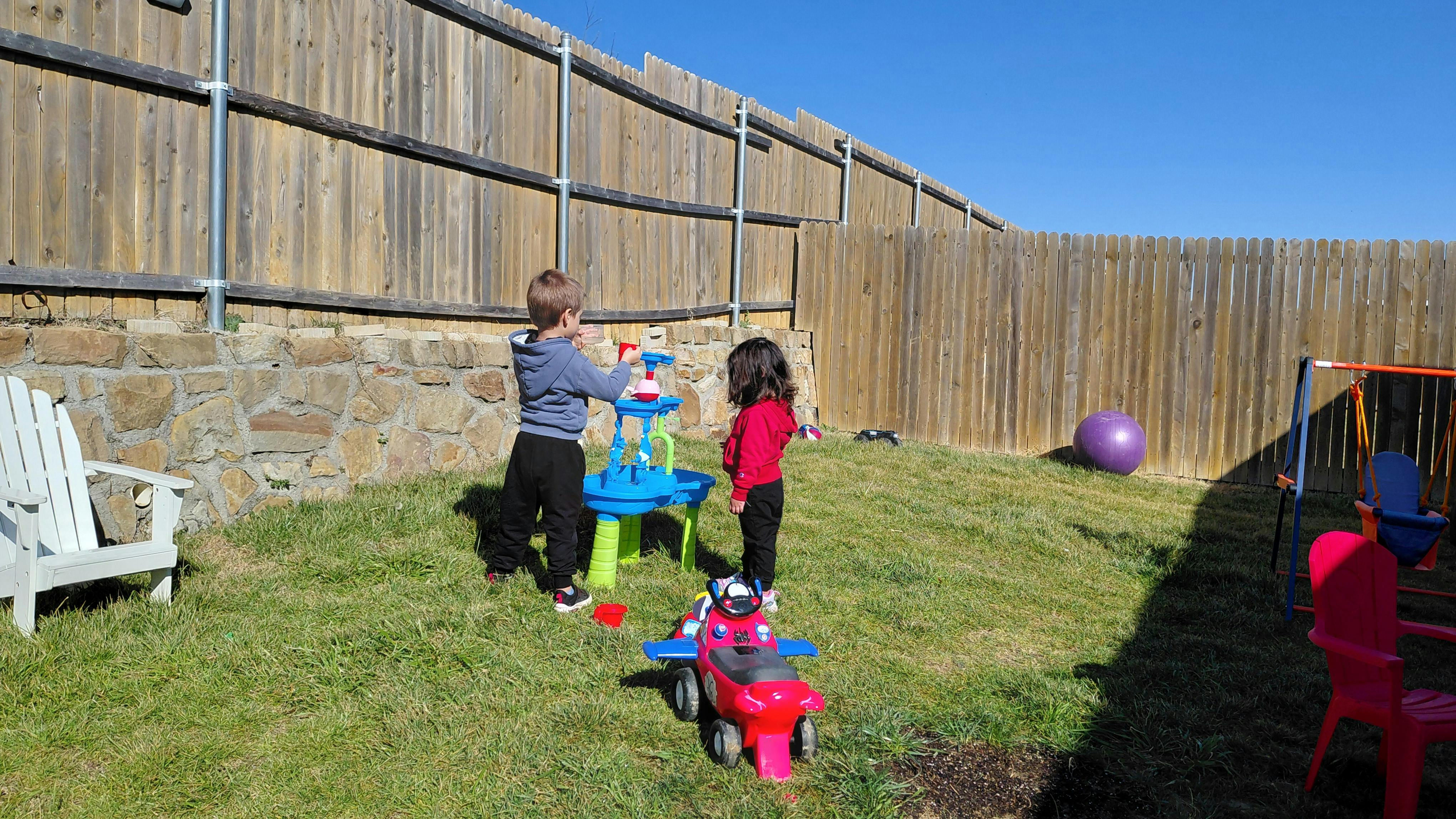 Two children playing with a water table in a grassy backyard