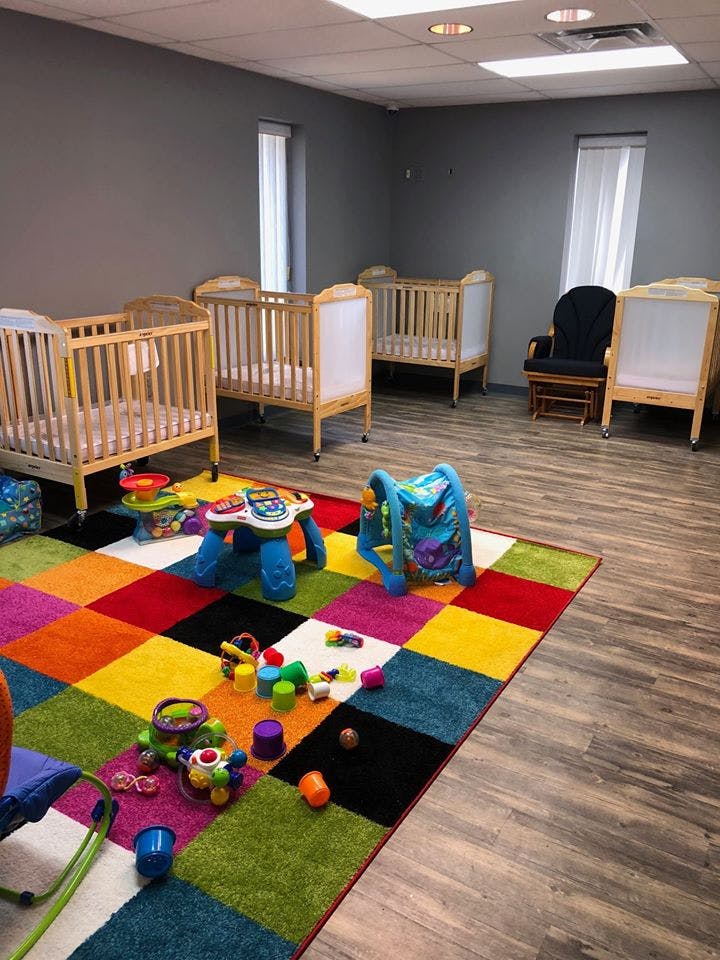 Nursery room with multiple cribs, a colorful rug, and toys