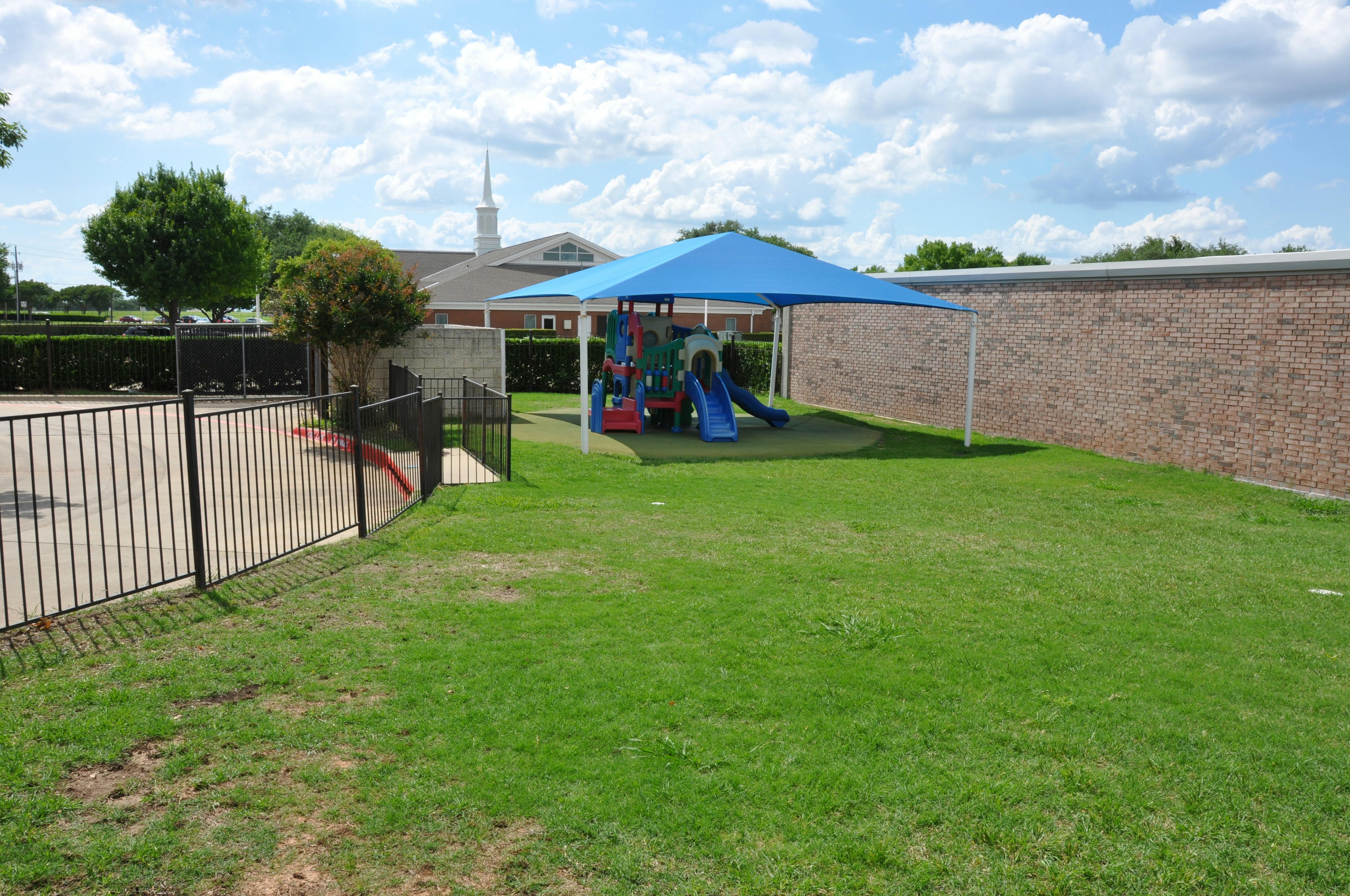 Playground structure with a blue shade canopy in a grass yard