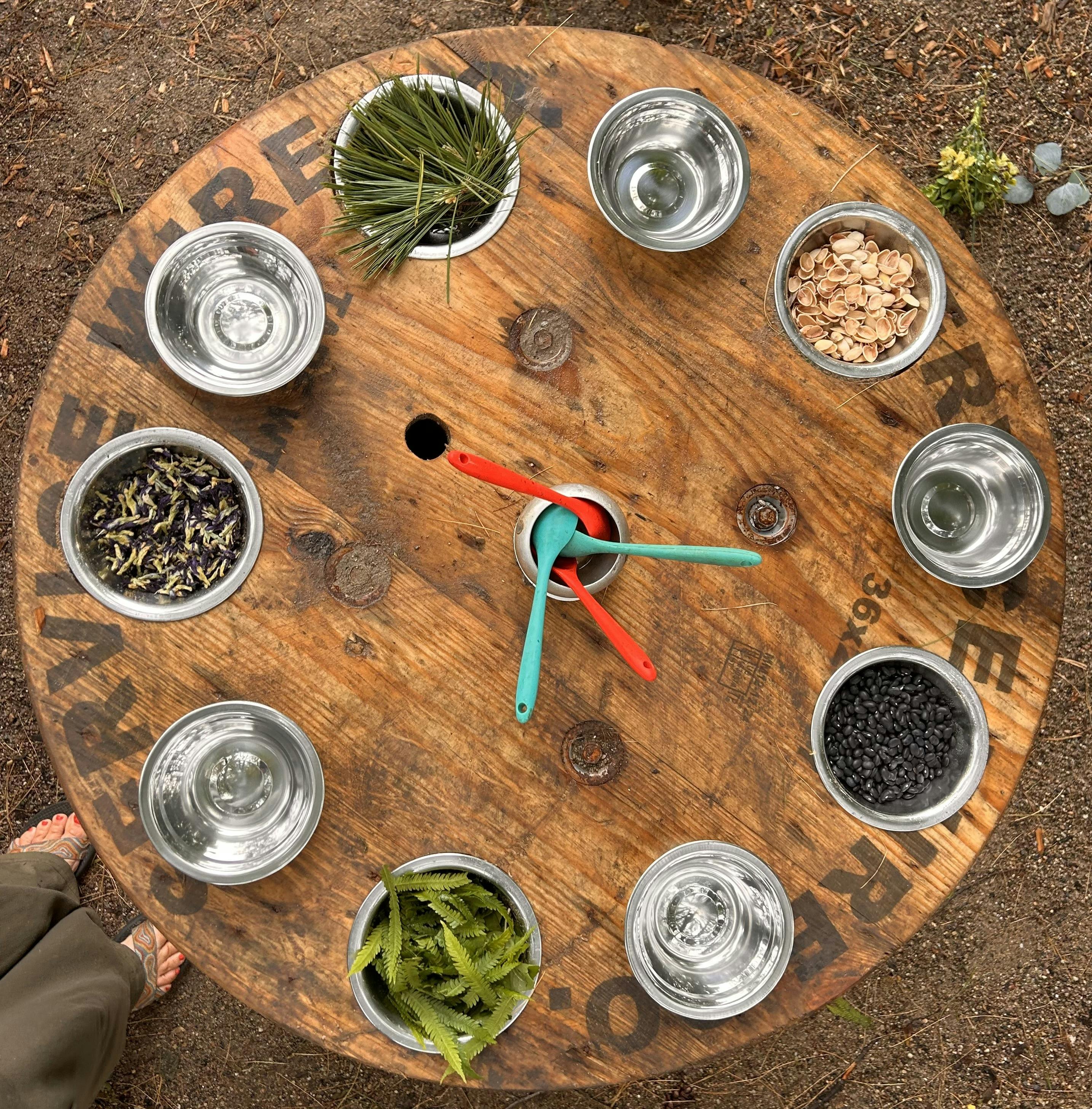 Wooden spool table with bowls of natural materials like beans, leaves, and pistachio shells