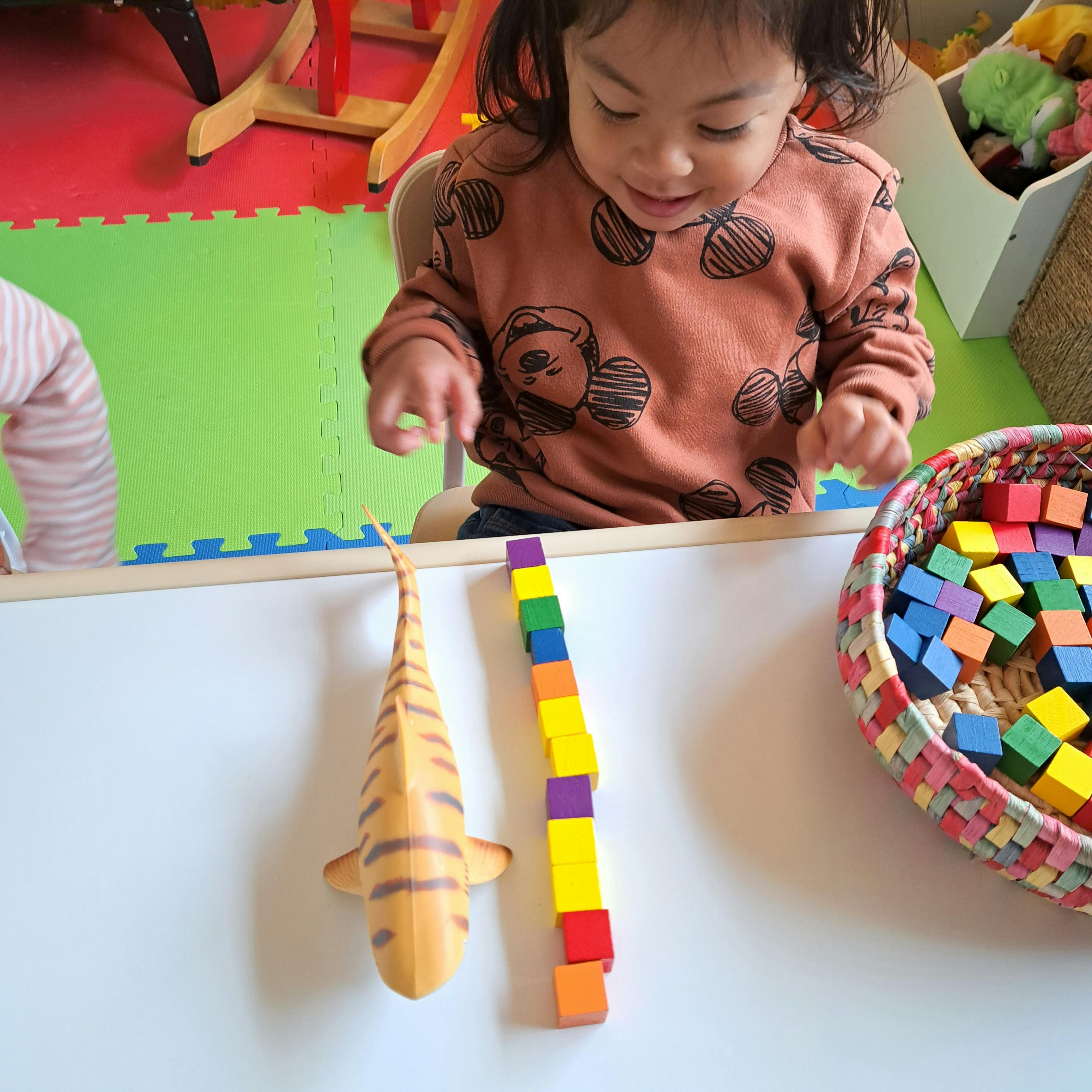 Child playing with colorful blocks and a toy fish on a white surface