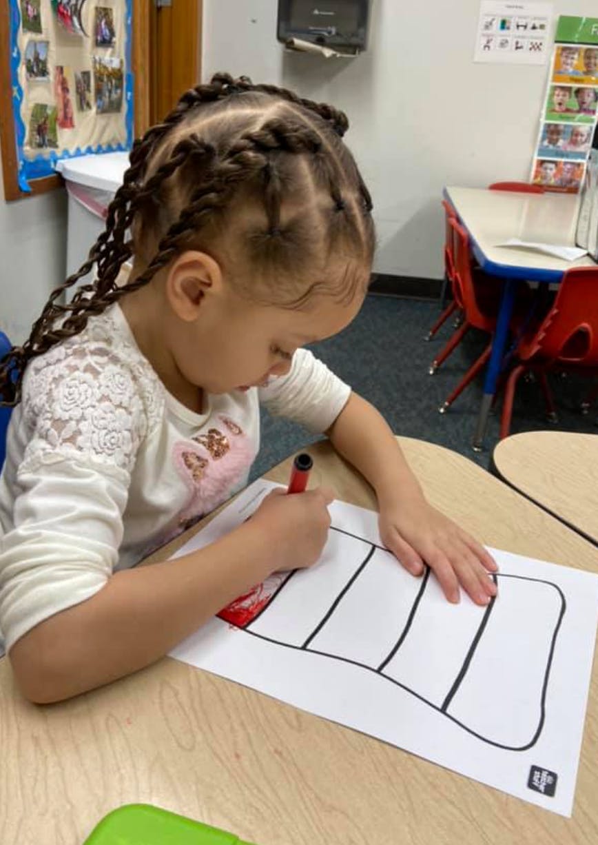 Child coloring a drawing of a striped hat in a classroom