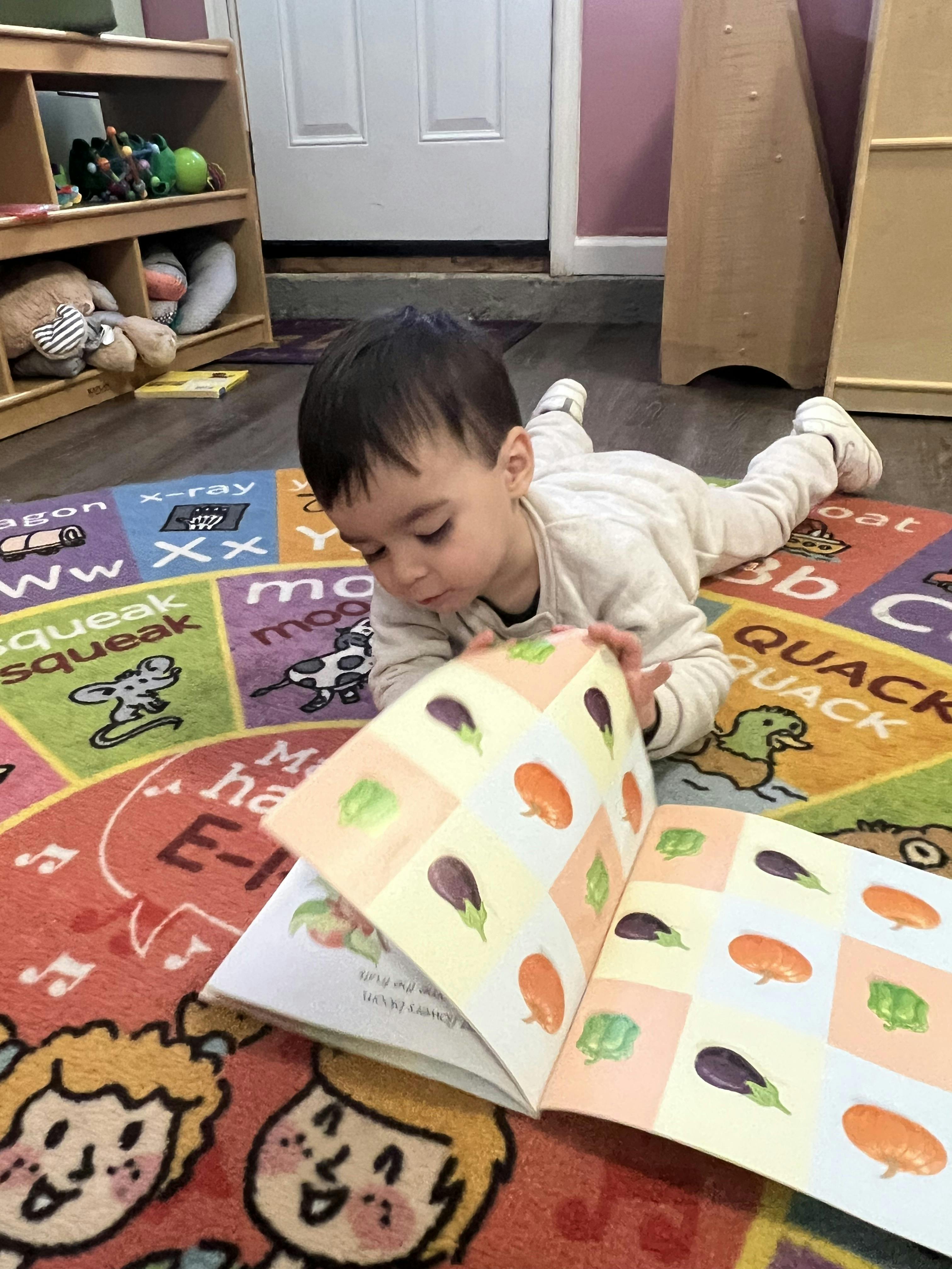 Child lying on a colorful rug, looking at a book