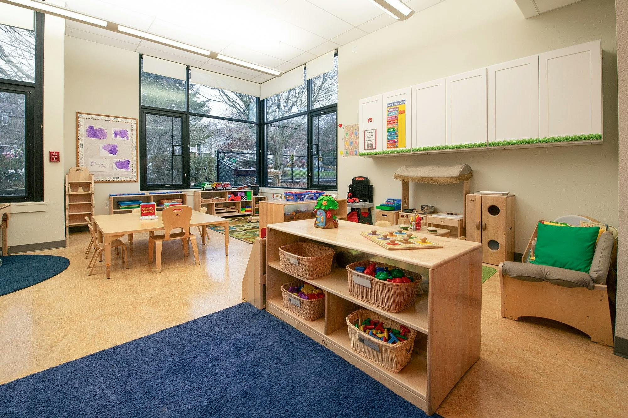 Empty classroom with small tables, chairs, and shelves of toys