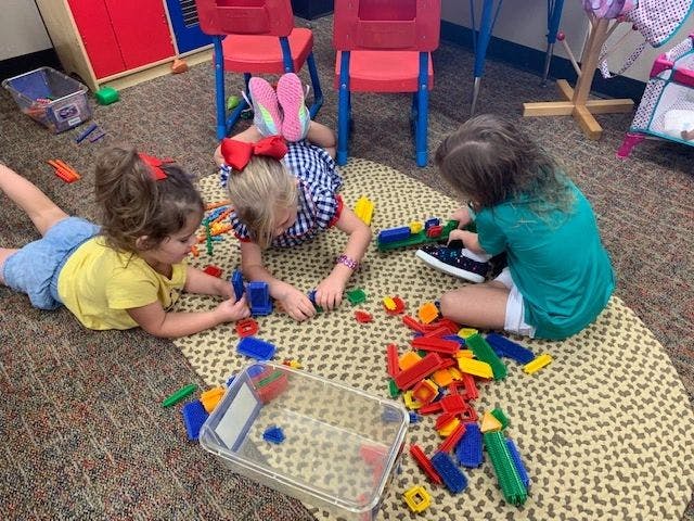 Three children playing with colorful building blocks on a rug