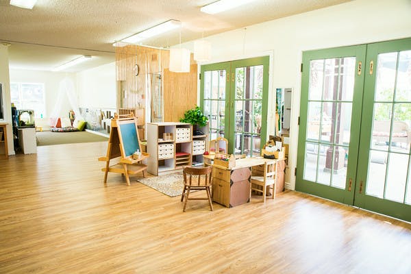 Classroom with small tables and chairs, an easel, and large green doors