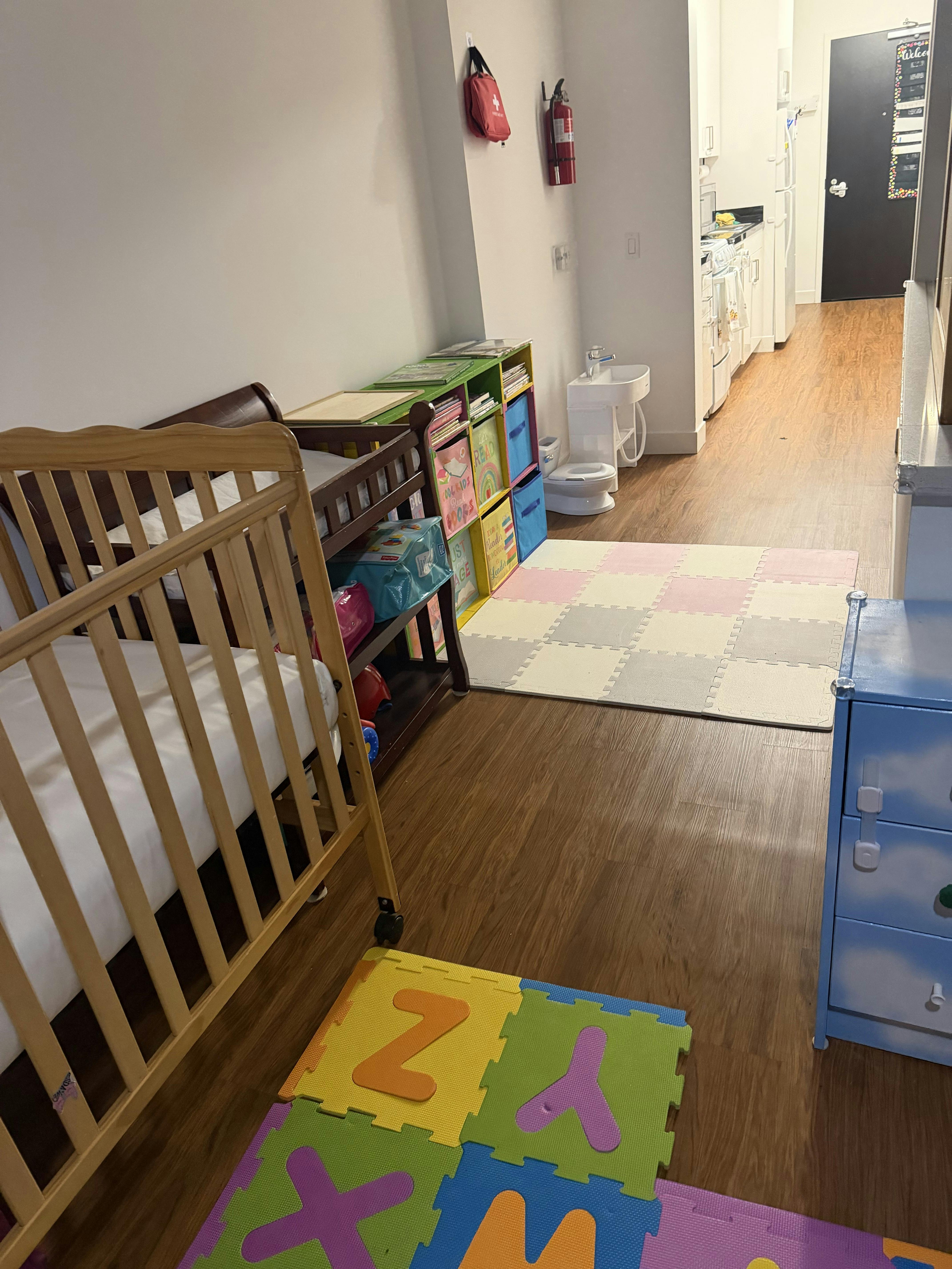 A room with a crib, changing table, shelves, and play mats on the floor