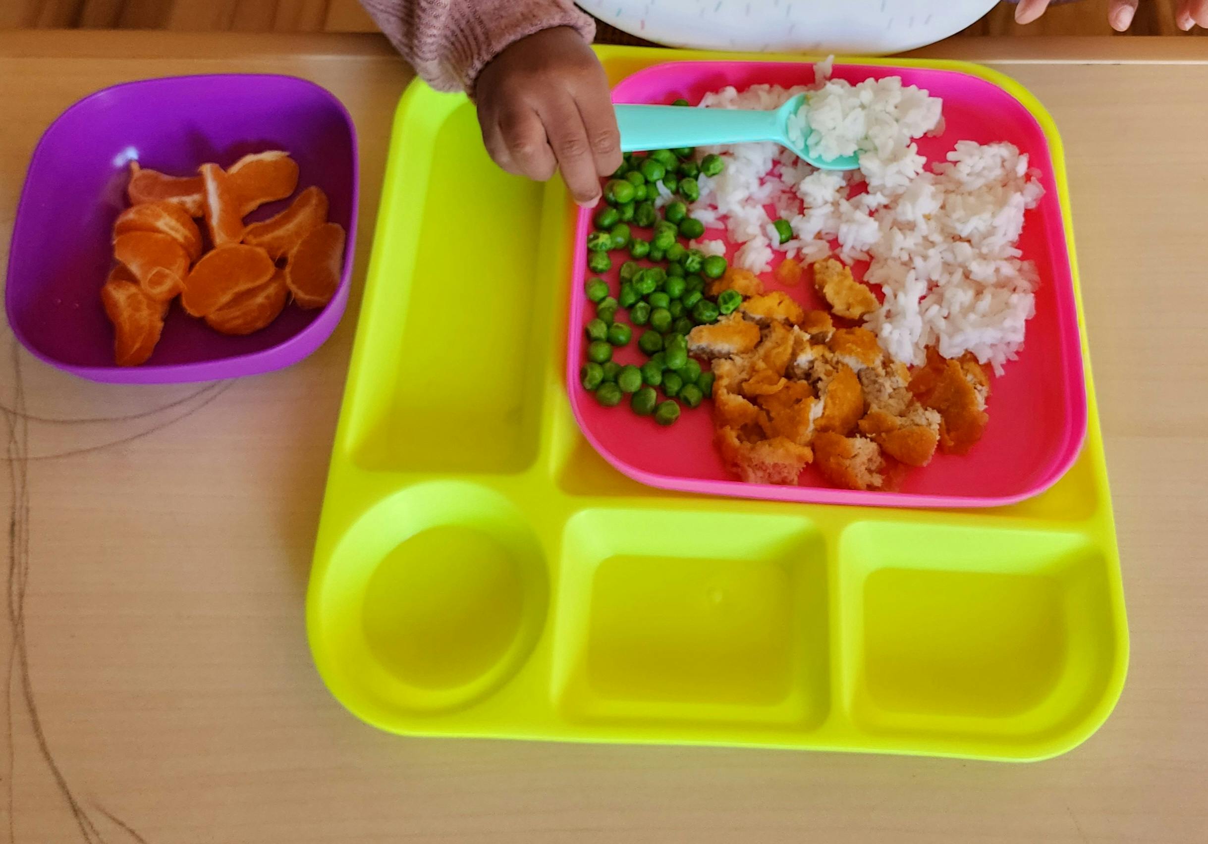 Child's hand holding a spoon over a plate of food
