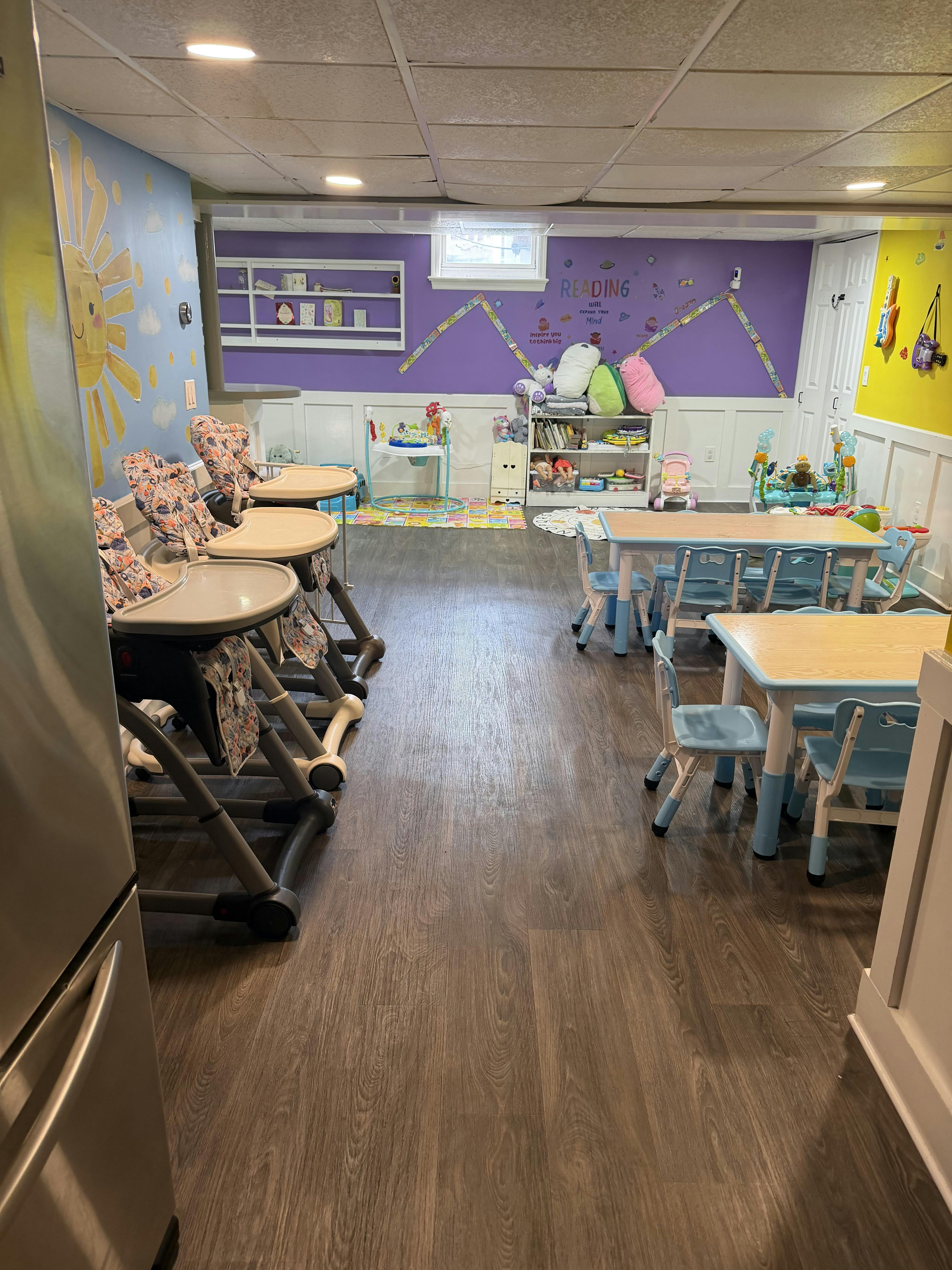Childcare room with high chairs, small tables, and toy storage shelves