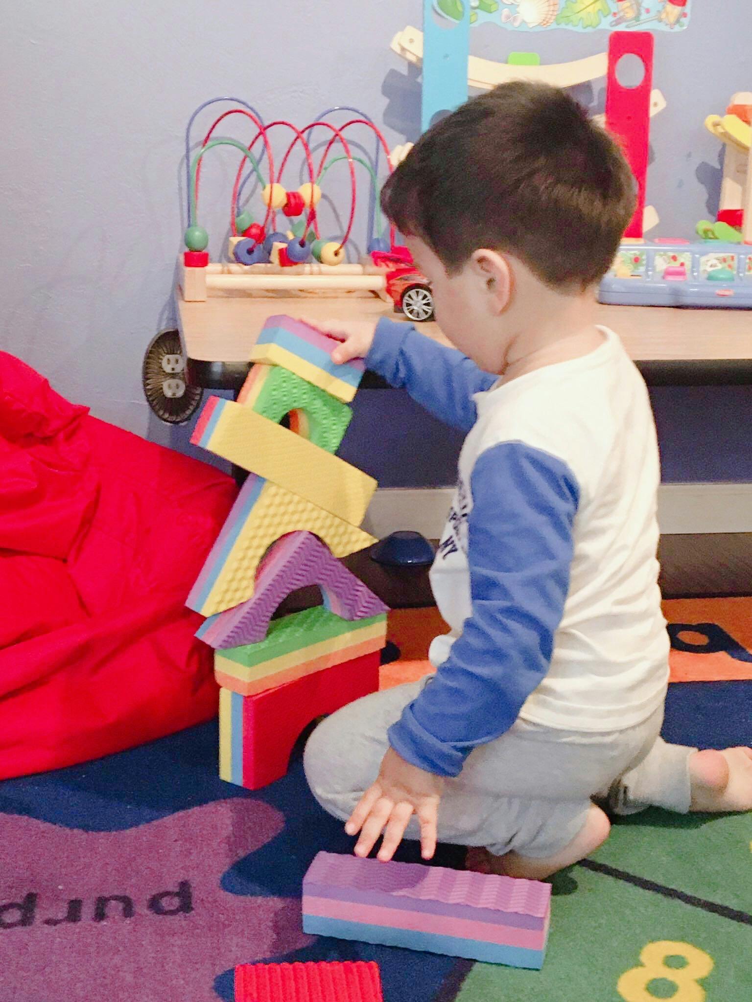 Child kneeling on a rug, playing with colorful building blocks