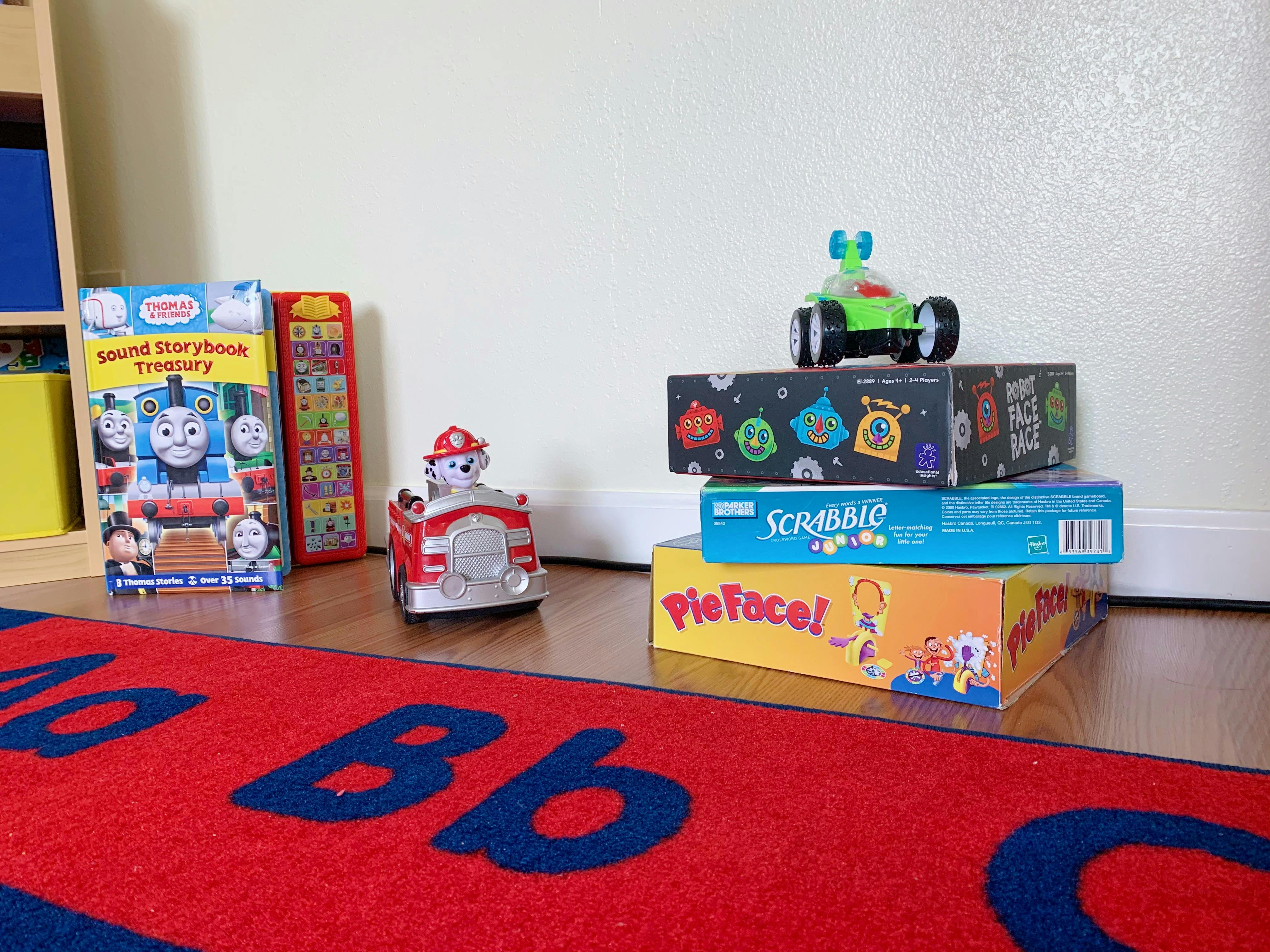 Children's books and board games on a wooden floor with a red rug
