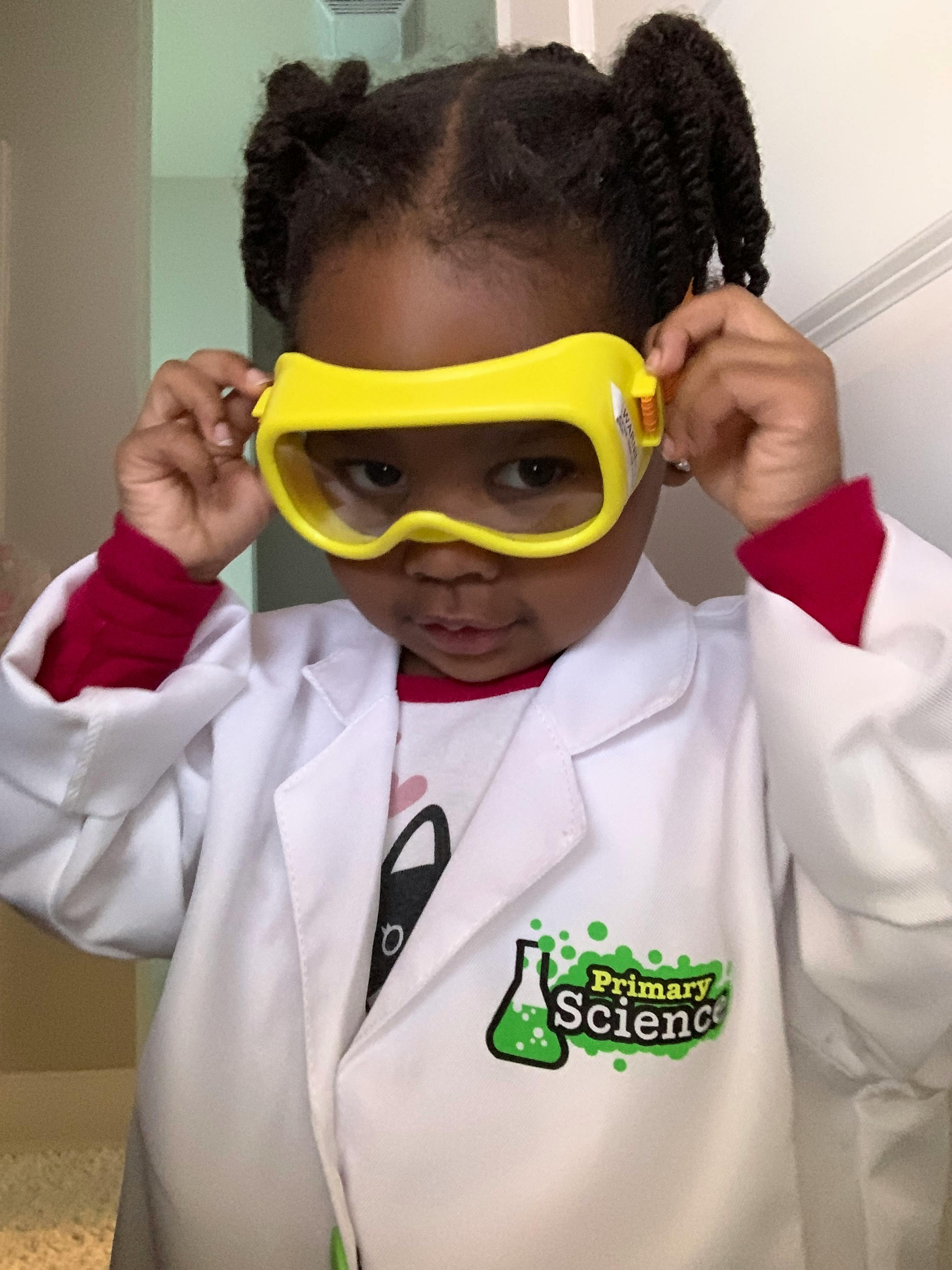 Child in a lab coat adjusting yellow safety goggles