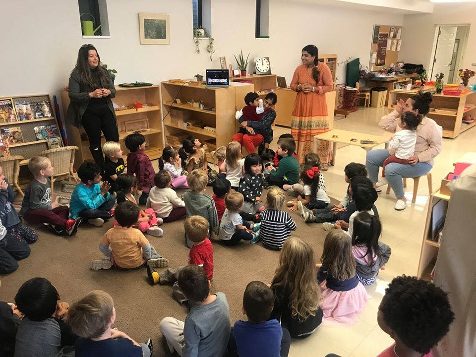 Two people standing in front of a group of children sitting on the floor in a classroom