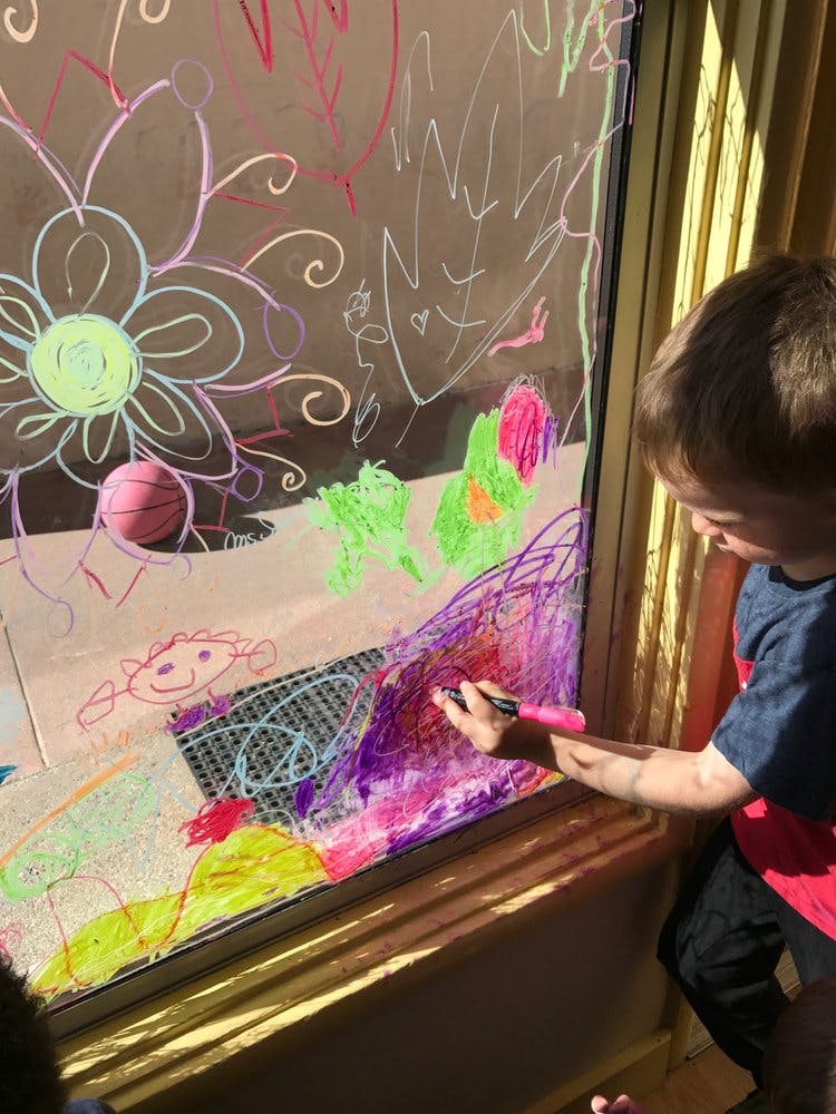 Child drawing on a window with colorful markers