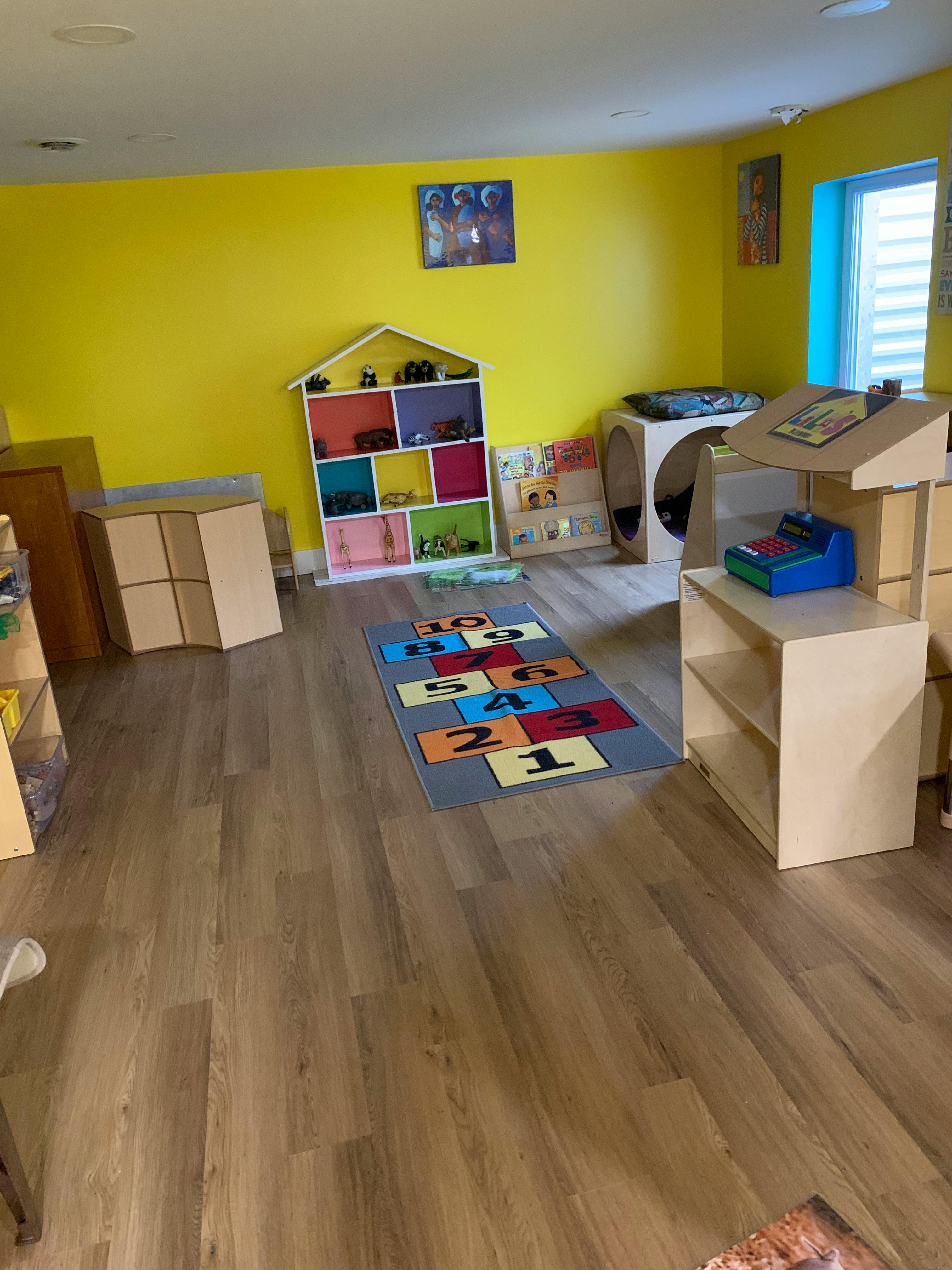 Playroom with yellow walls, a colorful hopscotch rug, and toy shelves