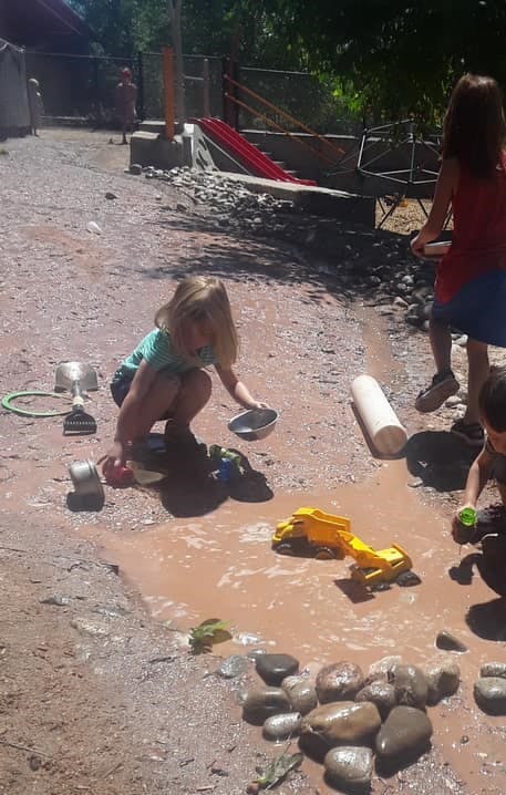 Child playing in a muddy puddle with toys