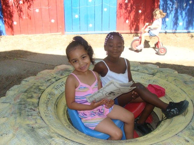Two children sitting in a tire, one holding a newspaper