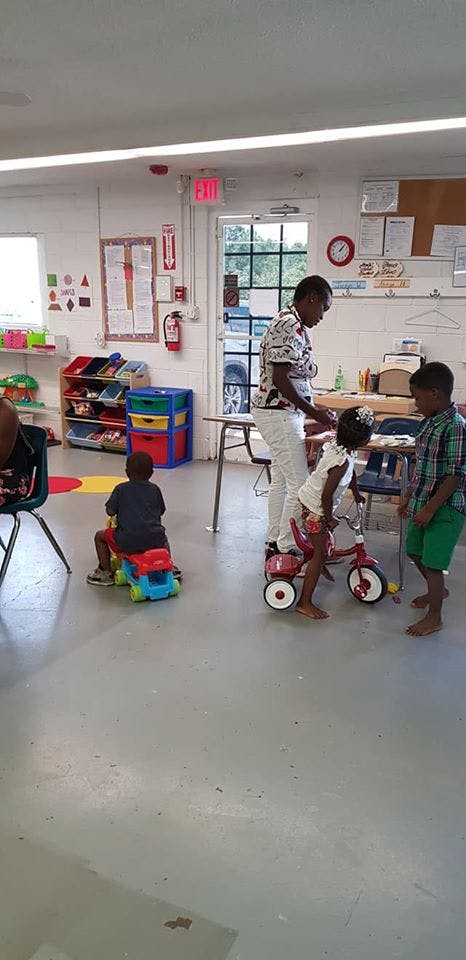 Adult and children in a classroom, one child on a ride-on toy