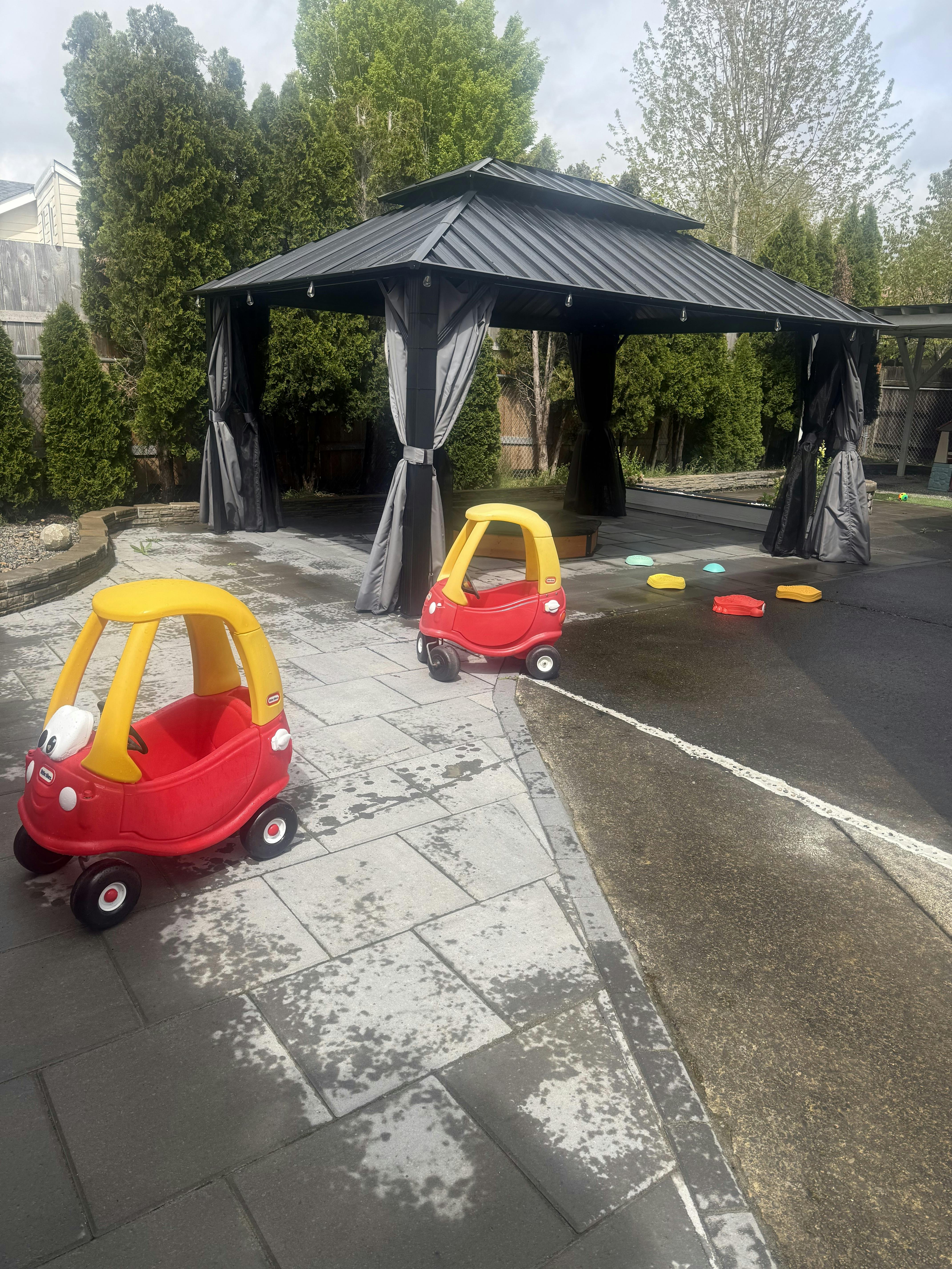 Two red and yellow toy cars on a patio next to a gazebo