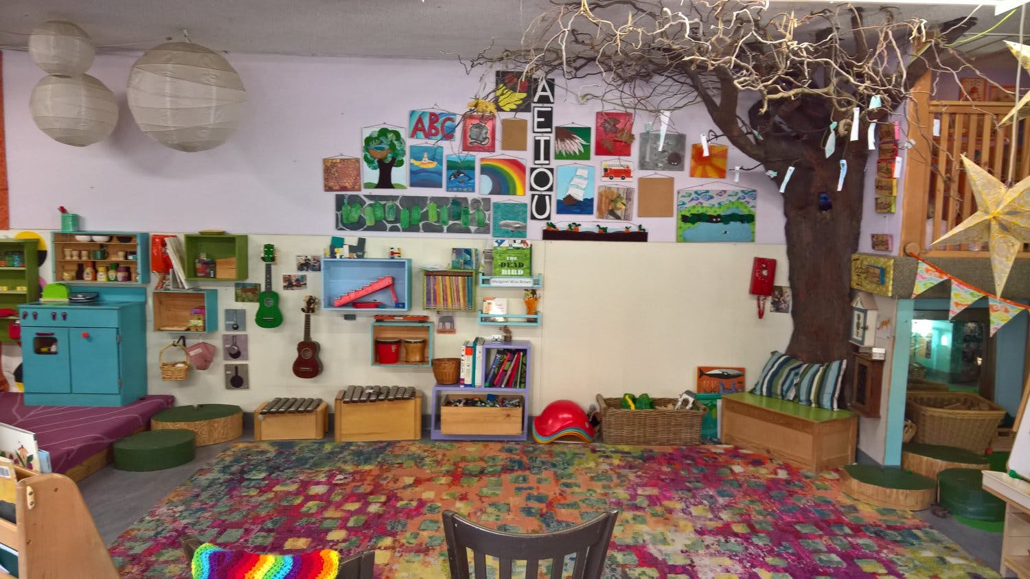 Children's play area with colorful rug, wall art, and a tree