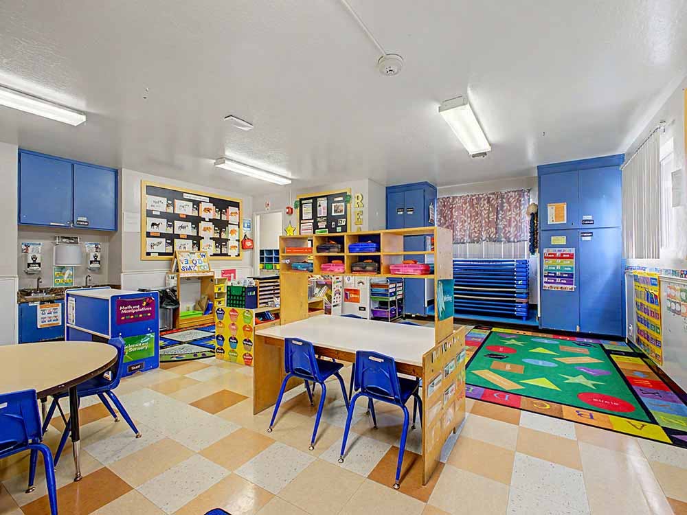 Colorful classroom with small tables and chairs, shelves, and a patterned rug