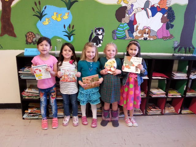 Five children holding books in front of a colorful wall mural