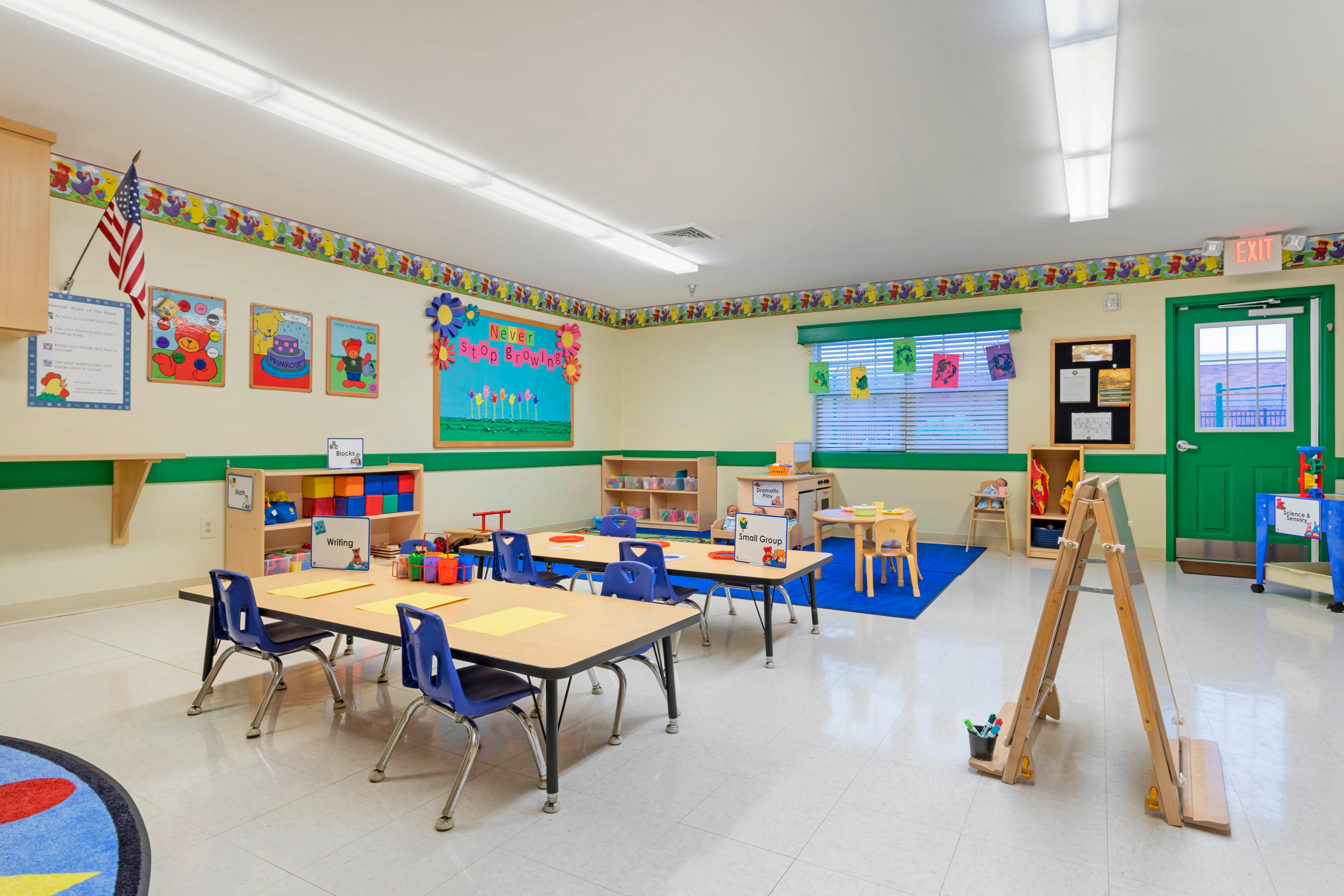 Empty classroom with small tables and chairs, shelves with toys