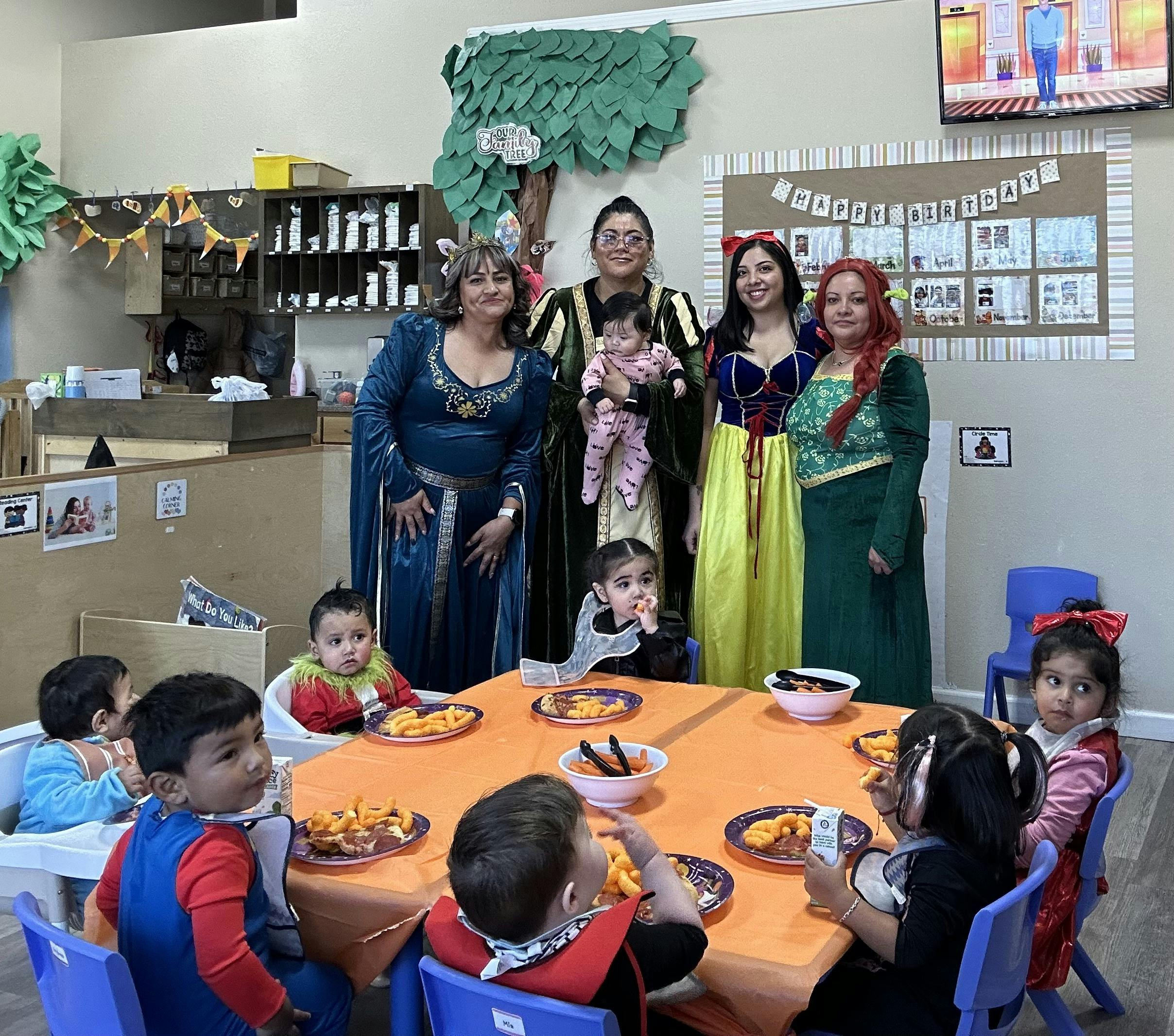Adults in costumes with children at a table with snacks