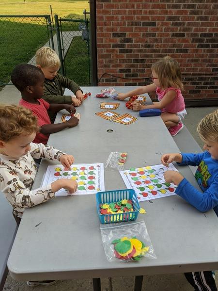 Children doing apple-themed learning activities at a picnic table