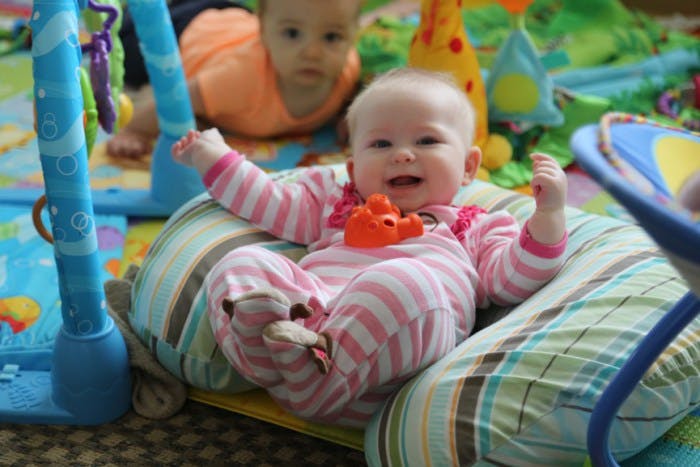 Child in striped pajamas sitting in a baby seat, another child in background