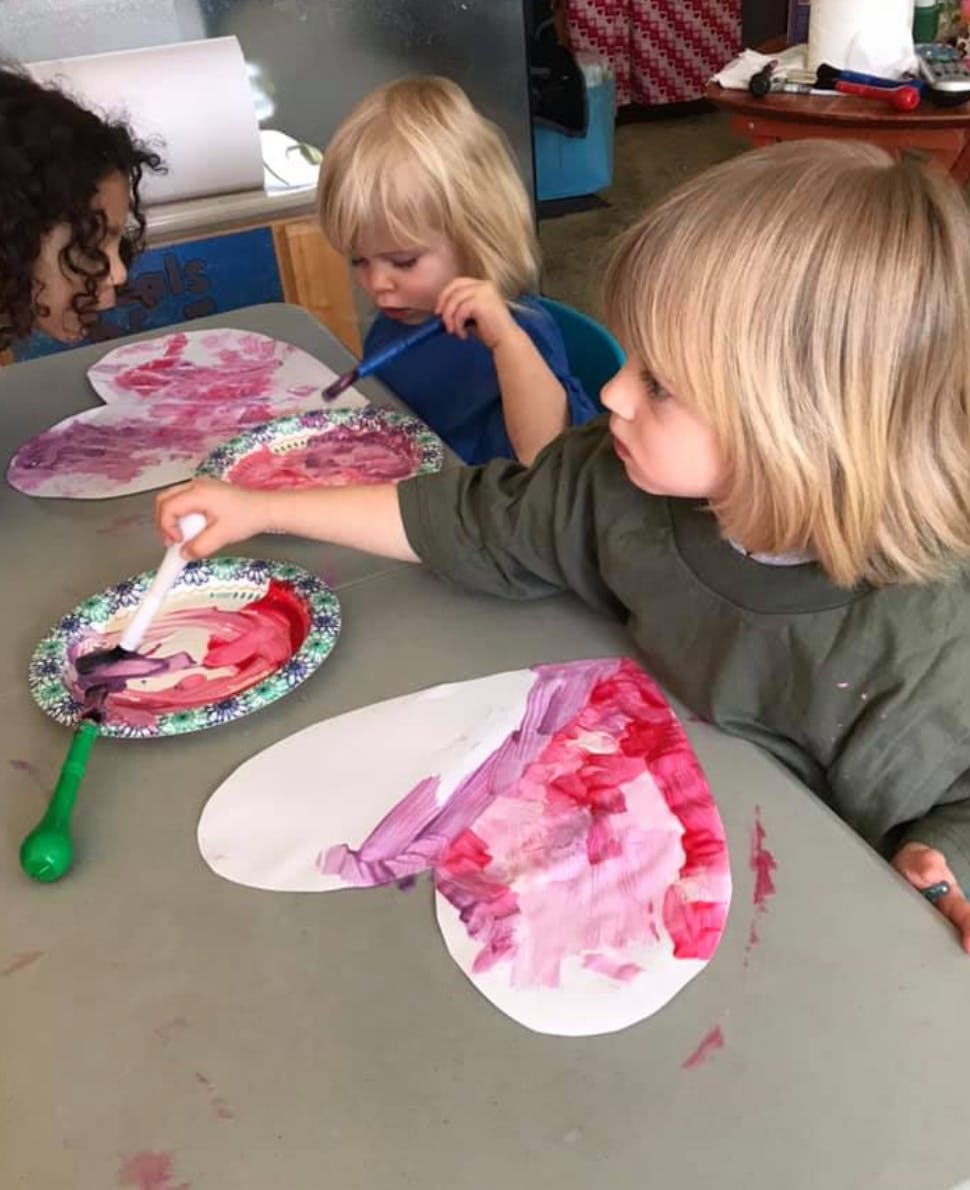 Three children painting paper cutouts at a table