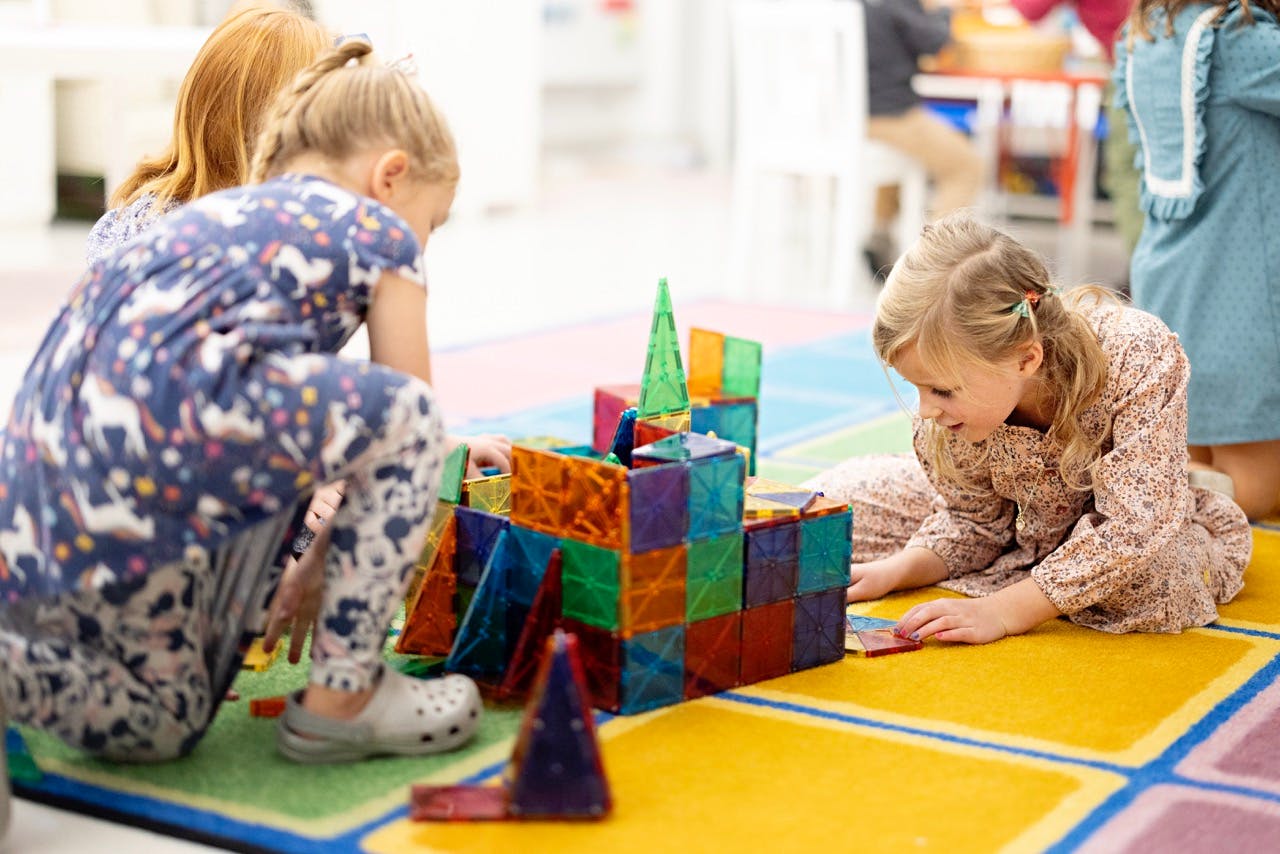 Two children playing with colorful magnetic blocks on a patterned rug