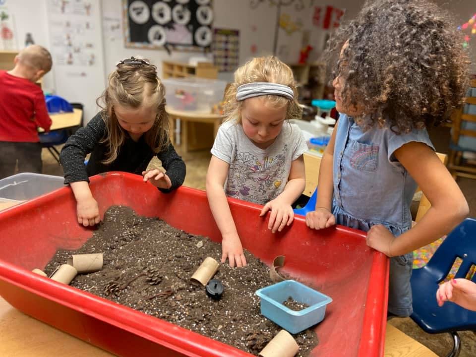 Three children playing with dirt in a red bin