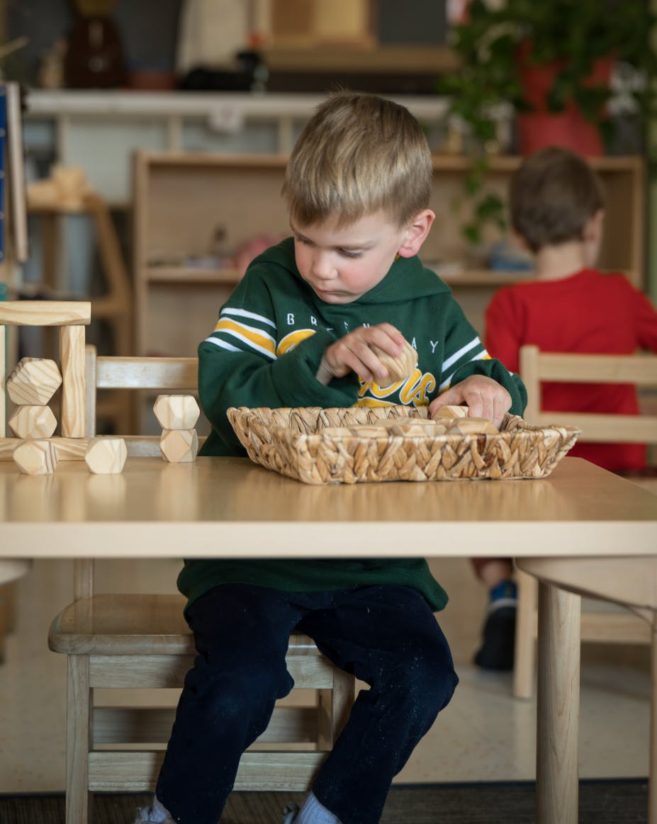 Child playing with wooden blocks at a table in a classroom