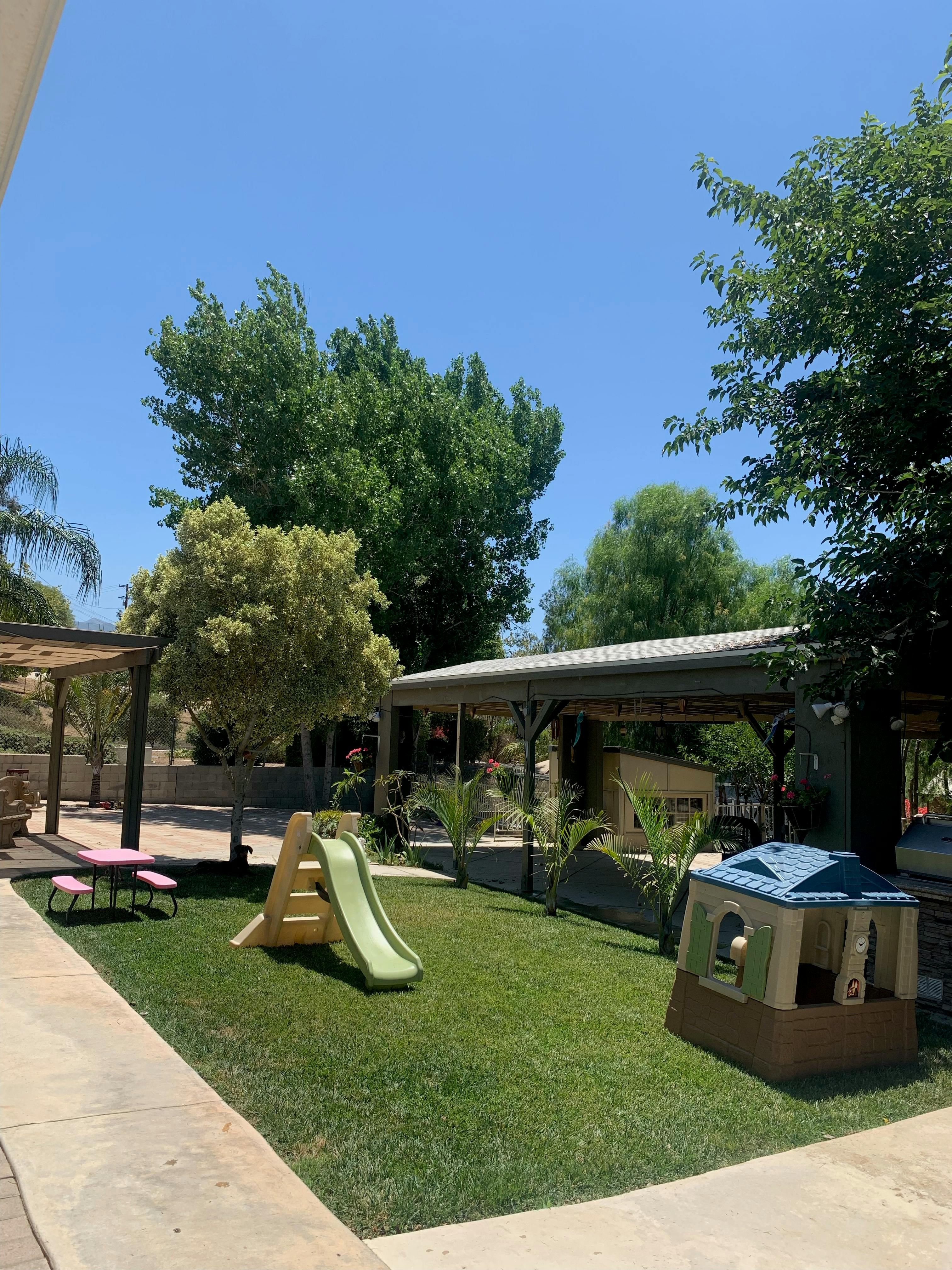Outdoor play area with a green slide, playhouse, and picnic table on grass