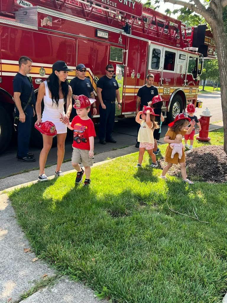 Children wearing plastic firefighter helmets standing near a parked fire truck
