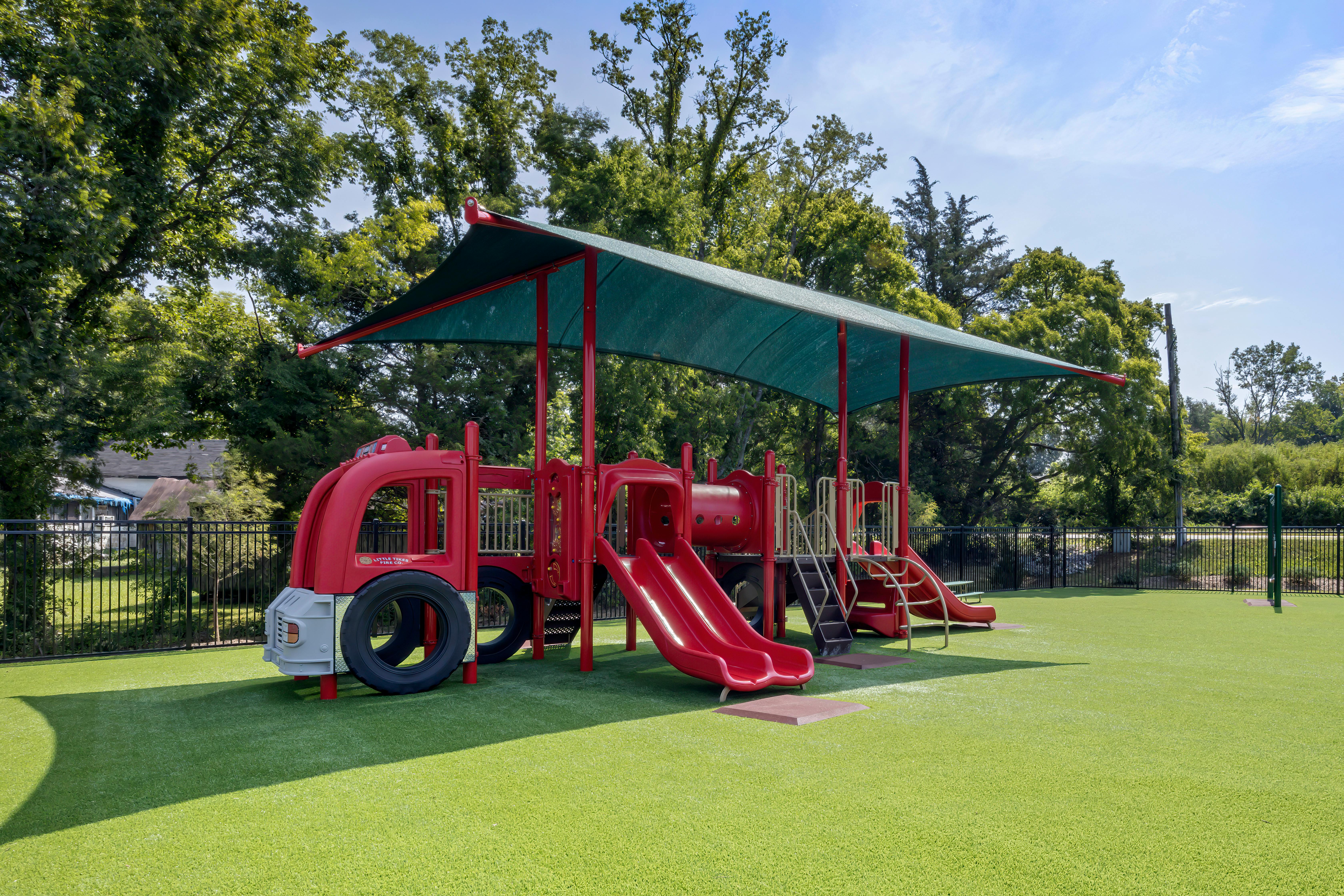 Red playground with slides and a fire truck-shaped play area on artificial green turf