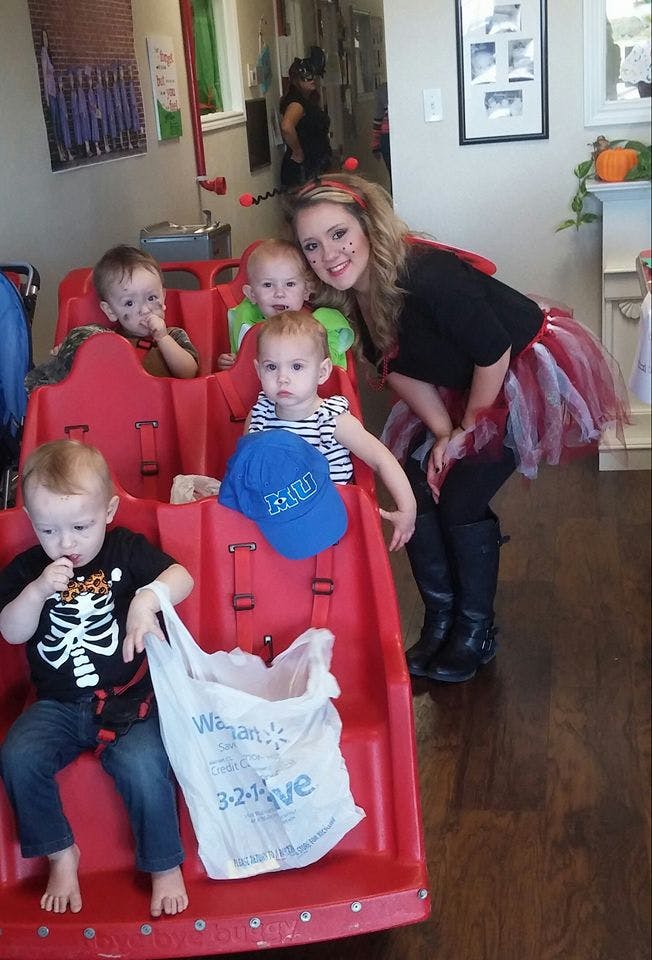 Person in costume with four children in a red wagon-seated cart