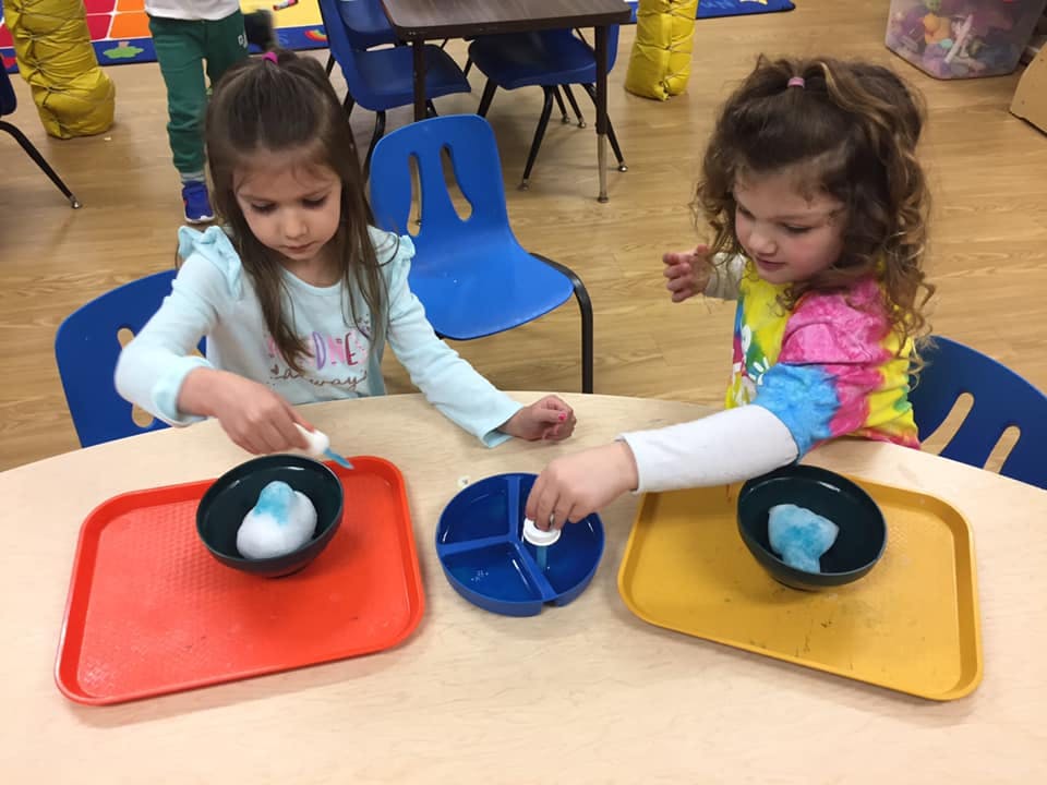 Two children at a table with trays and bowls, engaged in an activity