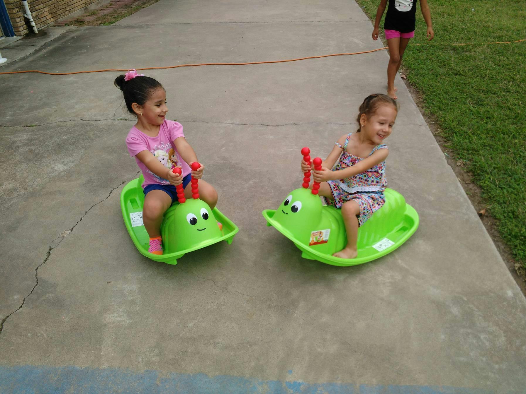 Two children riding green caterpillar rocking toys outdoors