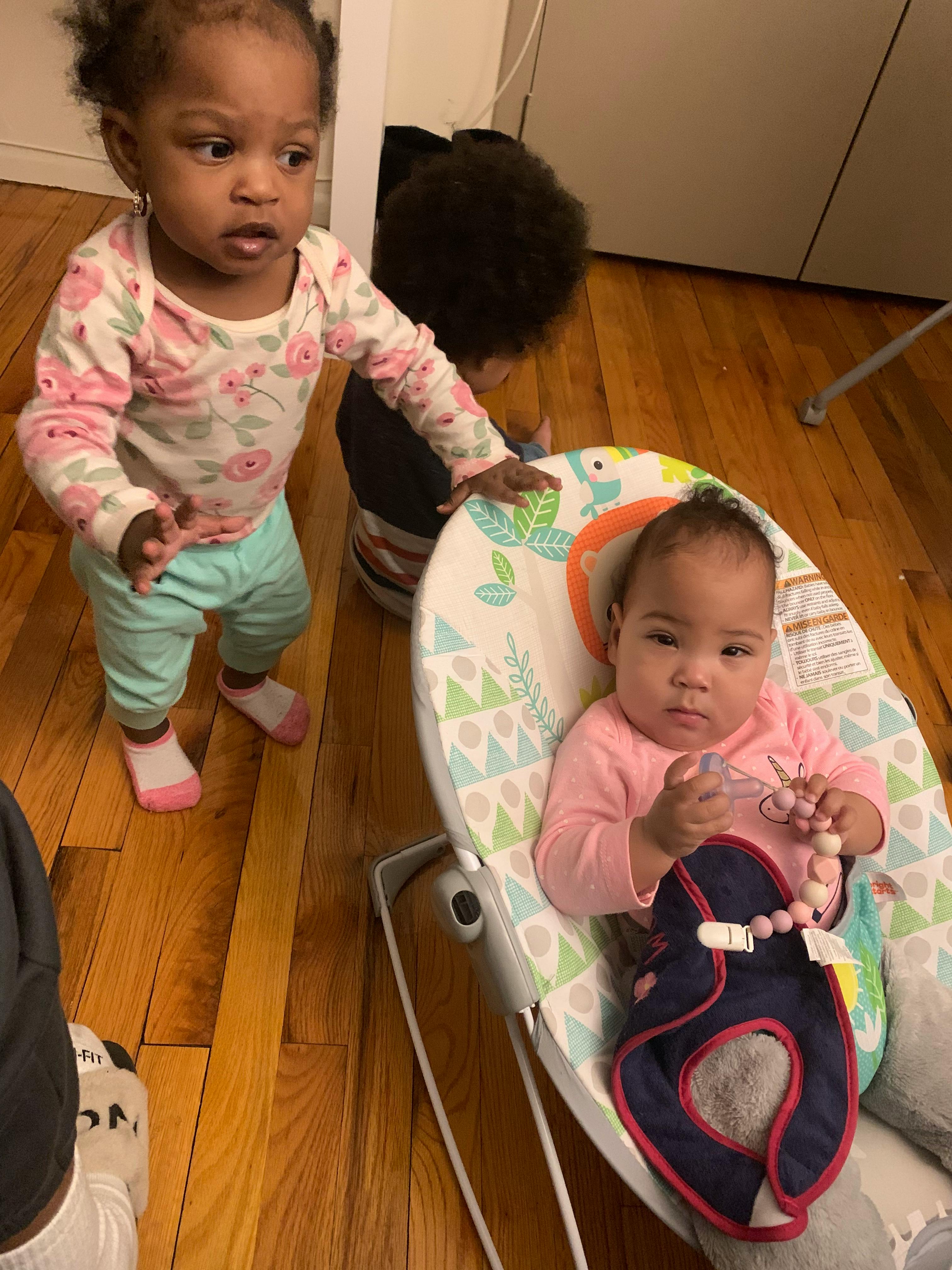 Child standing next to an infant in a bouncer