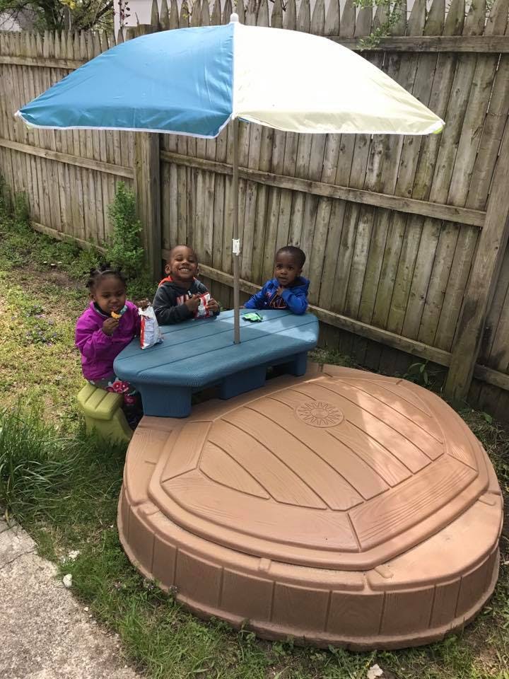 Three children sitting at a picnic table under an umbrella