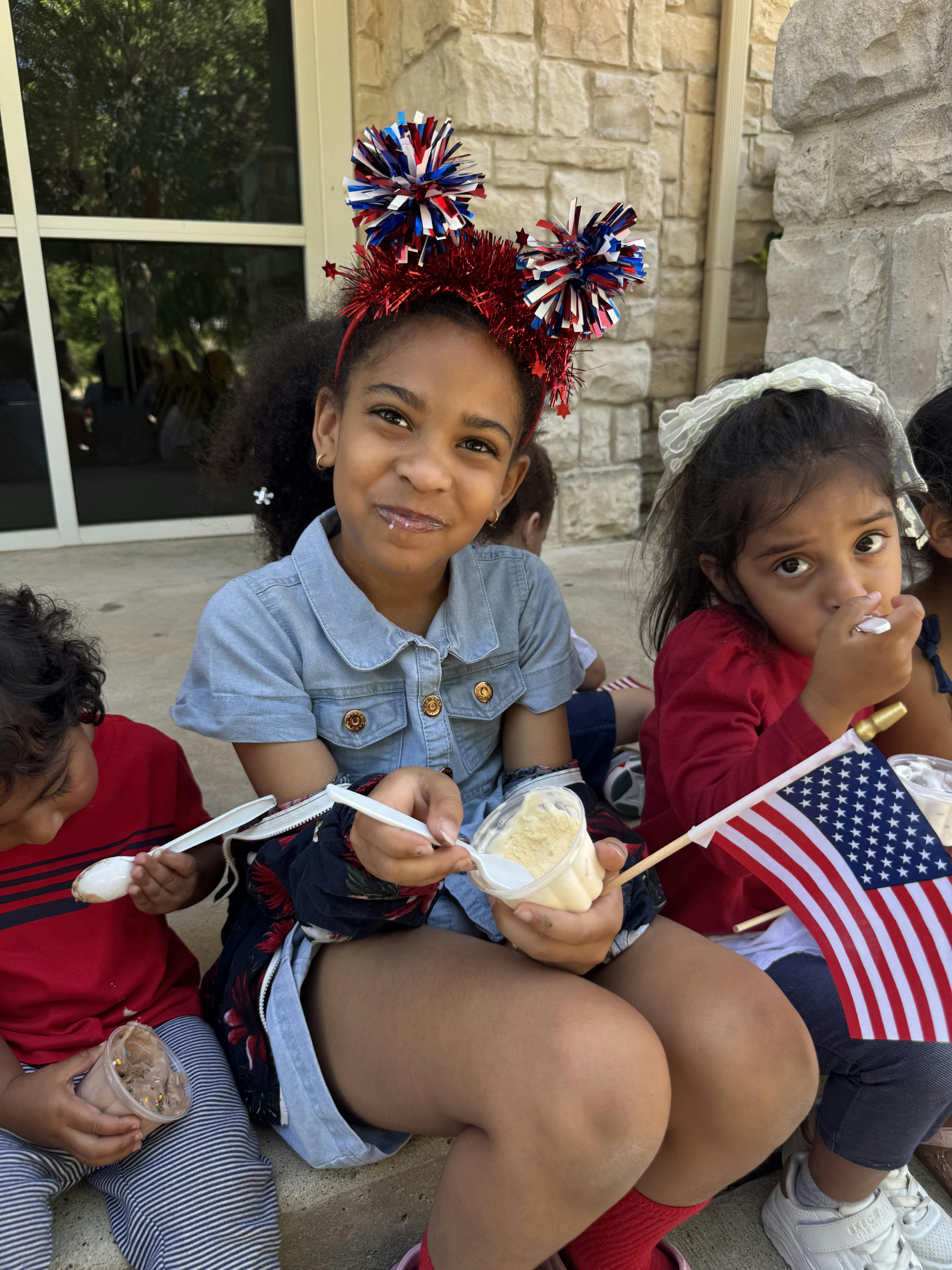 Children eating cups of ice cream while holding an American flag
