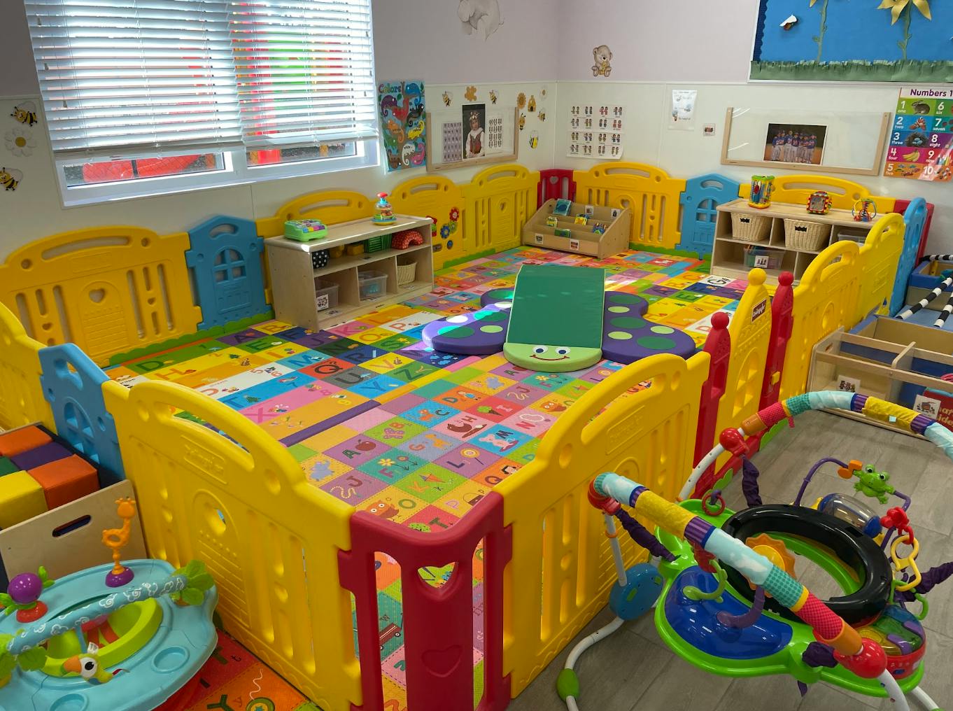 A colorful play area for young children with yellow fences and alphabet floor mats
