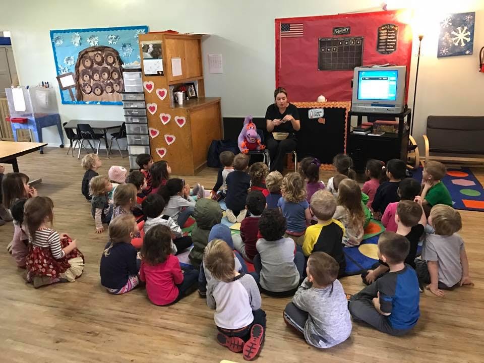 Adult leading a group of children sitting on the floor in a classroom