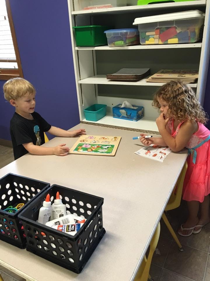 Two children at a table, one with a puzzle and one drawing