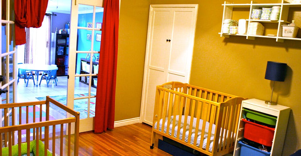 Two cribs in a room with a doorway leading to another room