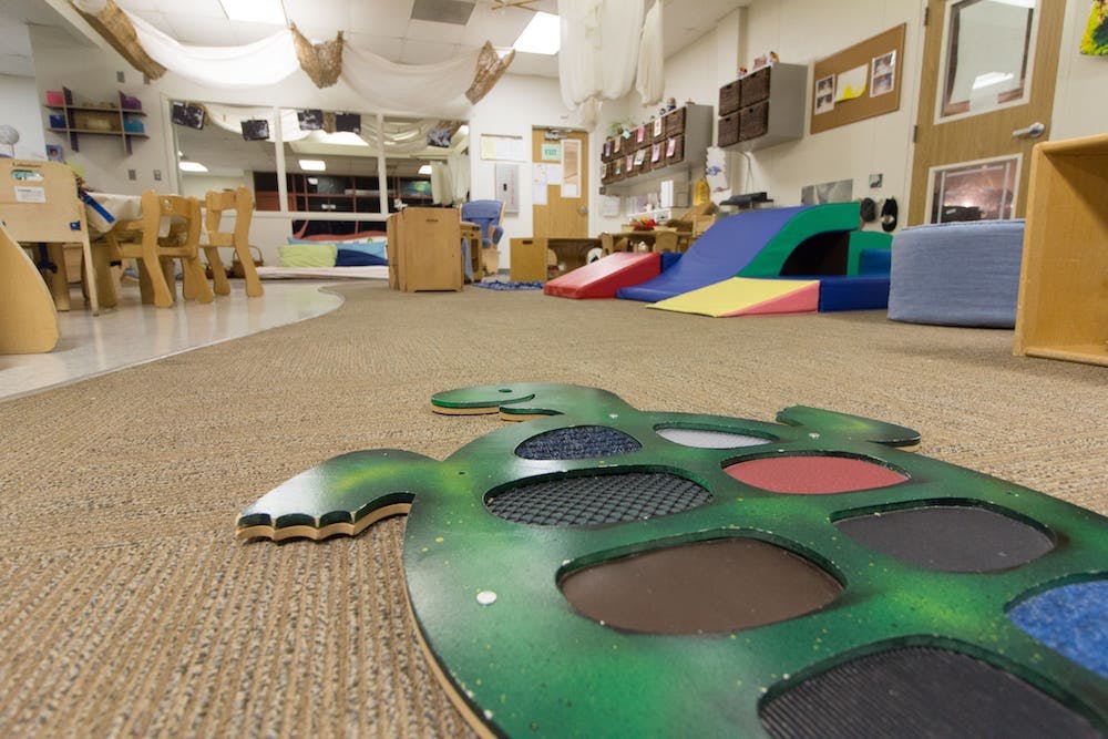 Green turtle-shaped mat with colorful textured circles on a carpeted floor in a classroom