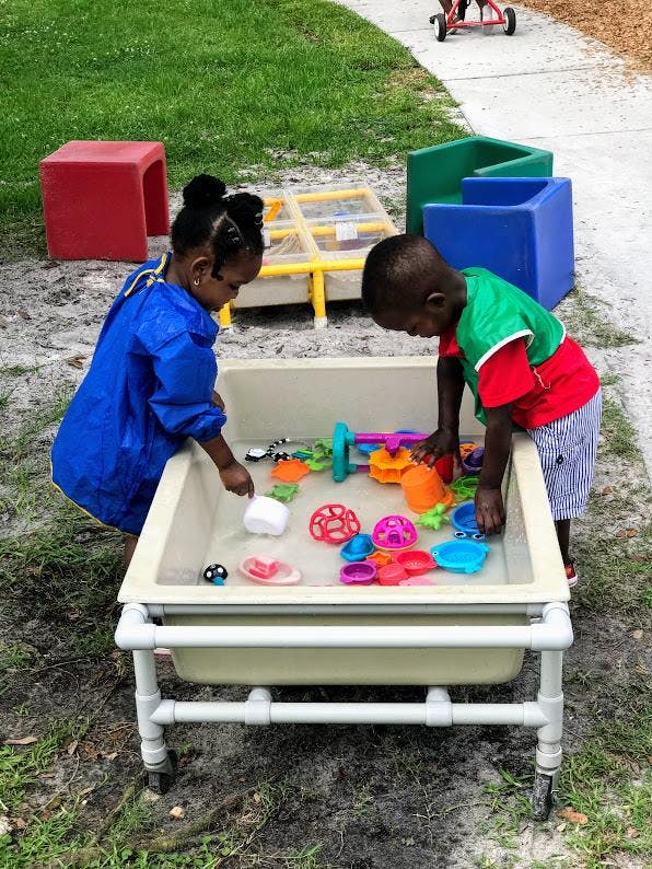 Two children playing with toys in a water table outdoors