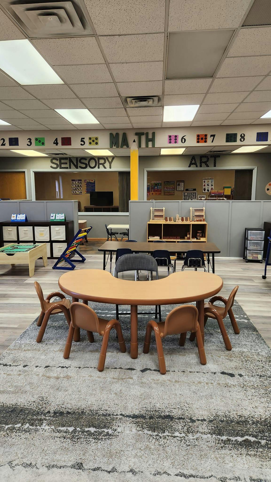 Classroom with small tables and chairs, signs for Math, Sensory, and Art